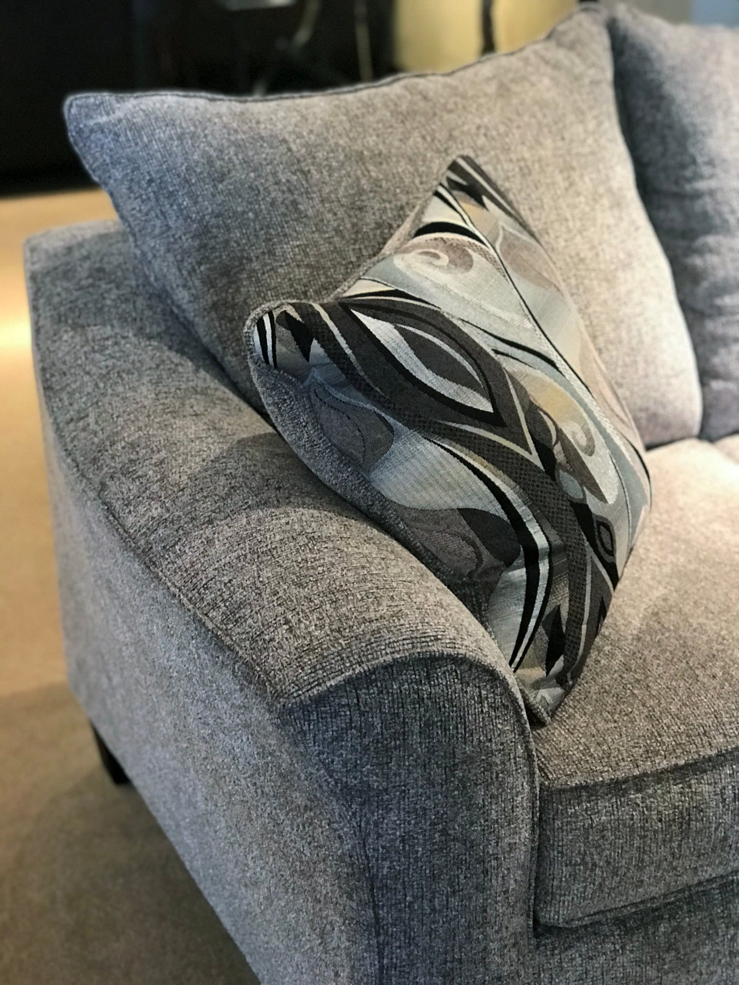 Close up of a grey textured fabric sofa with a decorative abstract pattern pillow