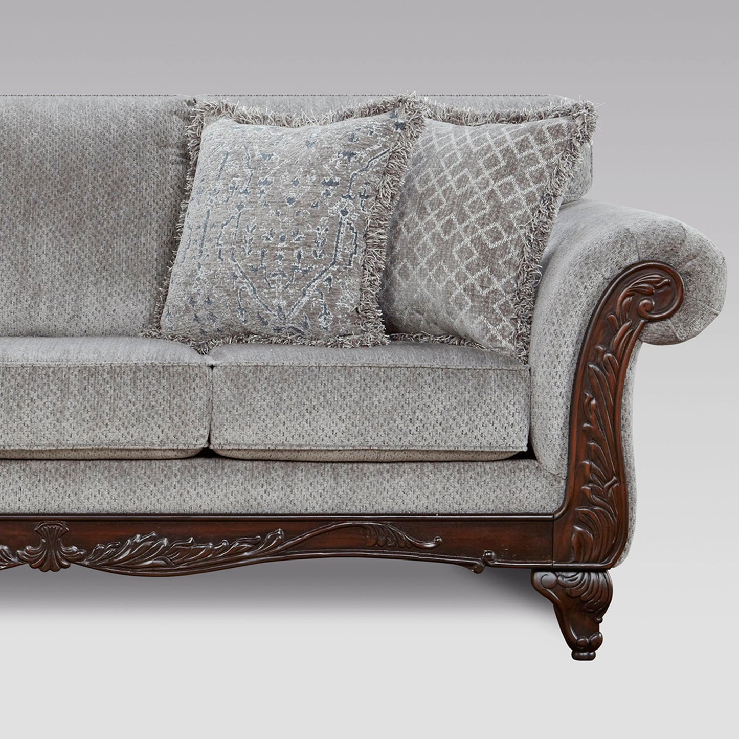 Grey fabric sofa with ornate carved wood armrest and fringe accent pillows