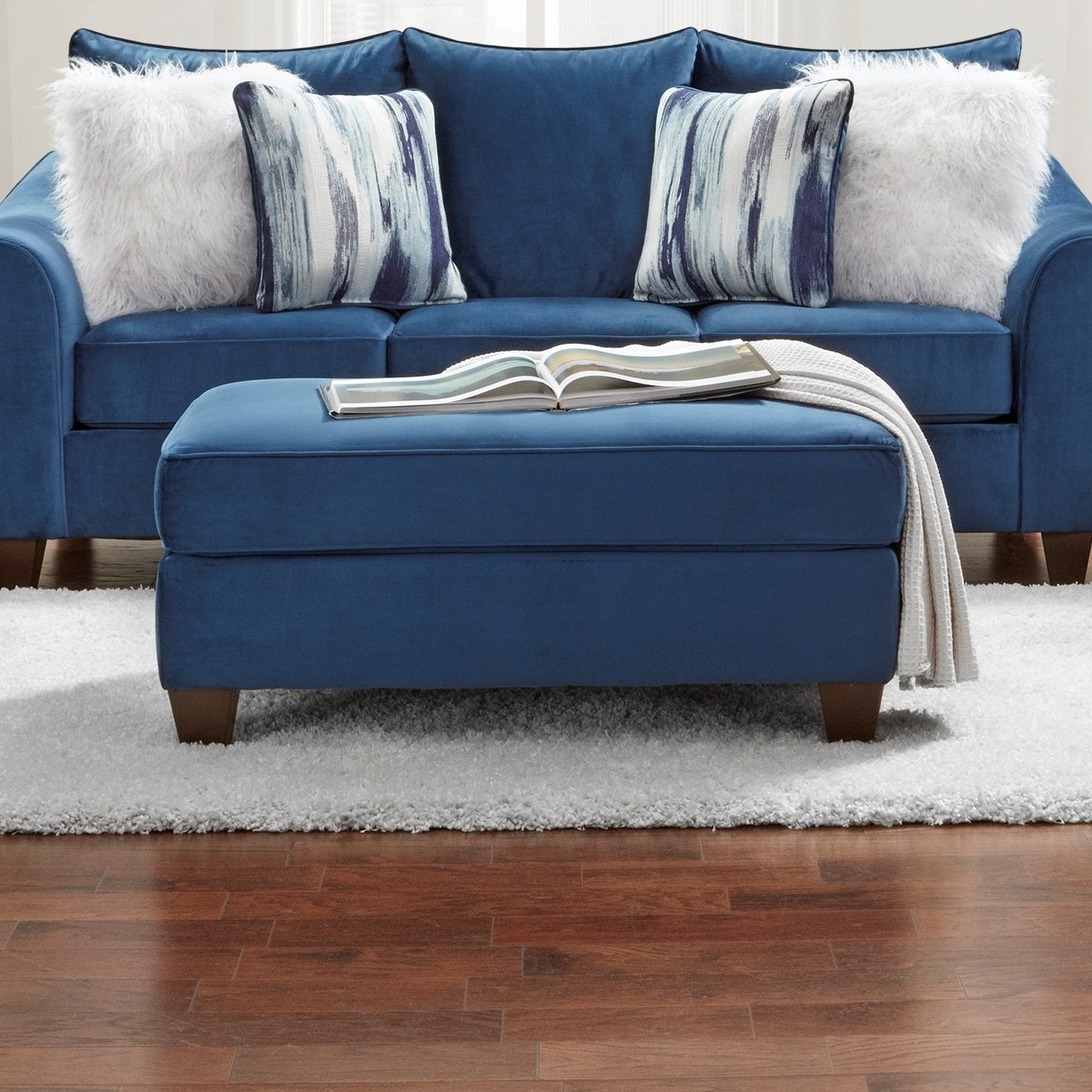 Plush navy blue velvet ottoman with a white throw blanket draped over the side