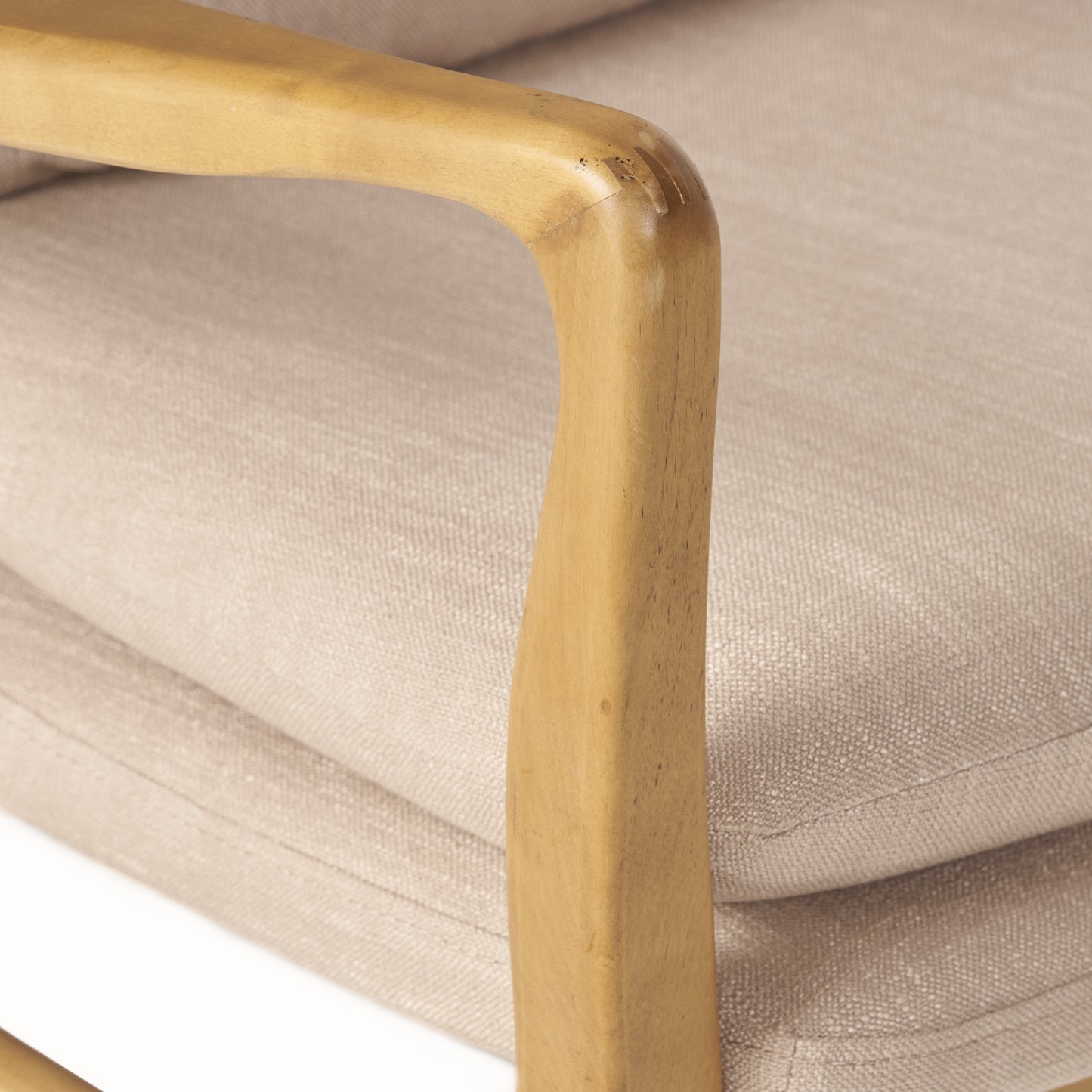 Closeup of a light beige fabric chair with a smooth wooden armrest