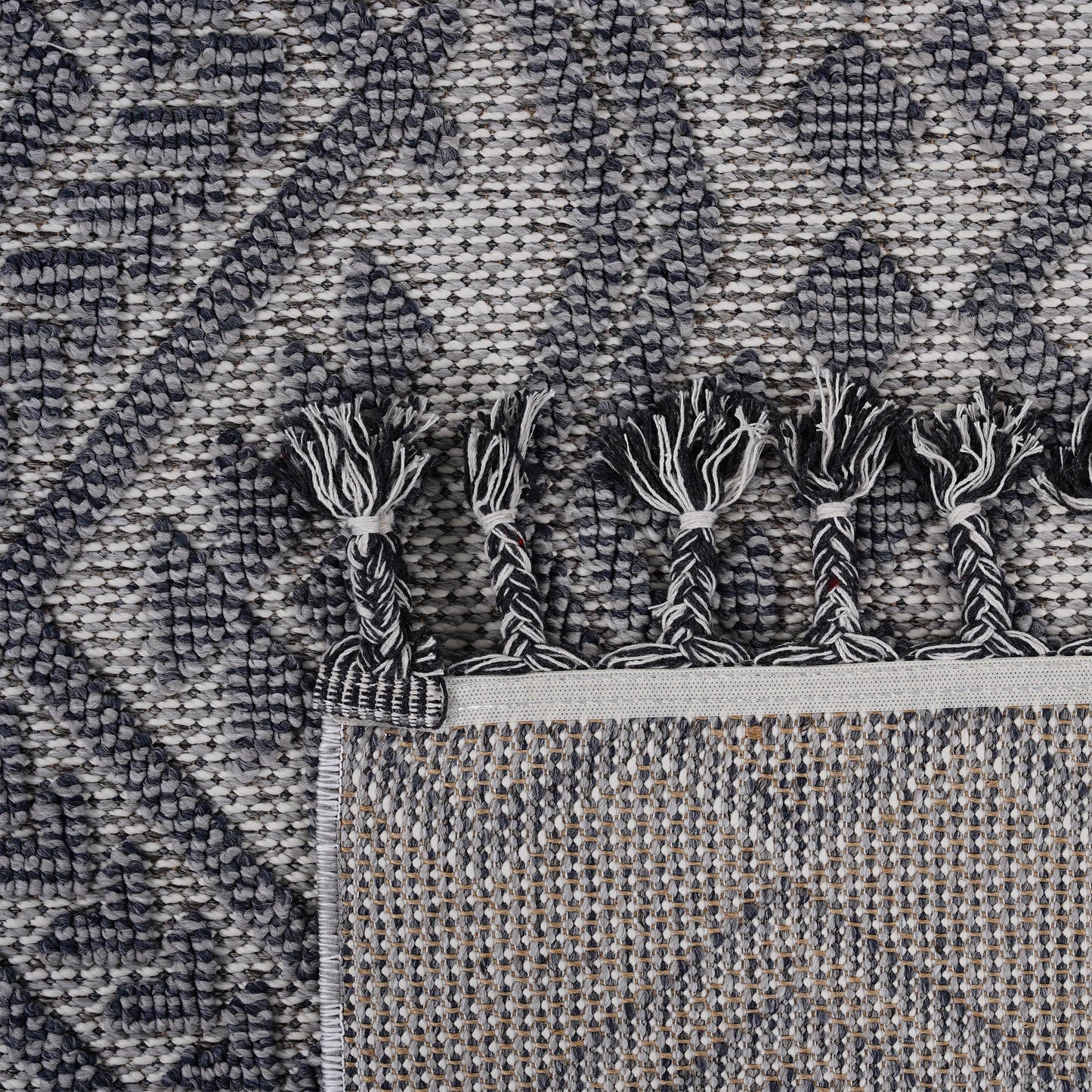 Closeup of a textured gray and white diamond pattern area rug with braided tassels