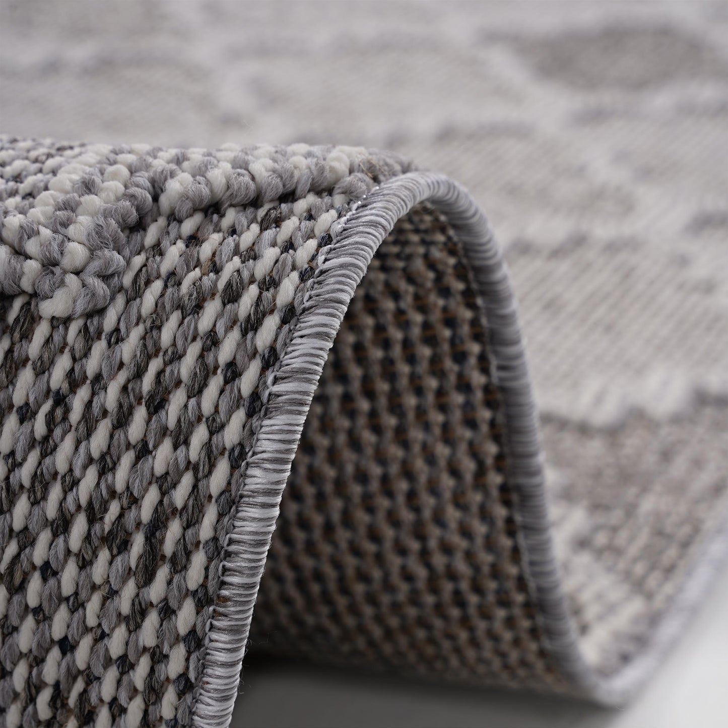 Closeup of a textured grey and white area rug with a geometric pattern and bound edge