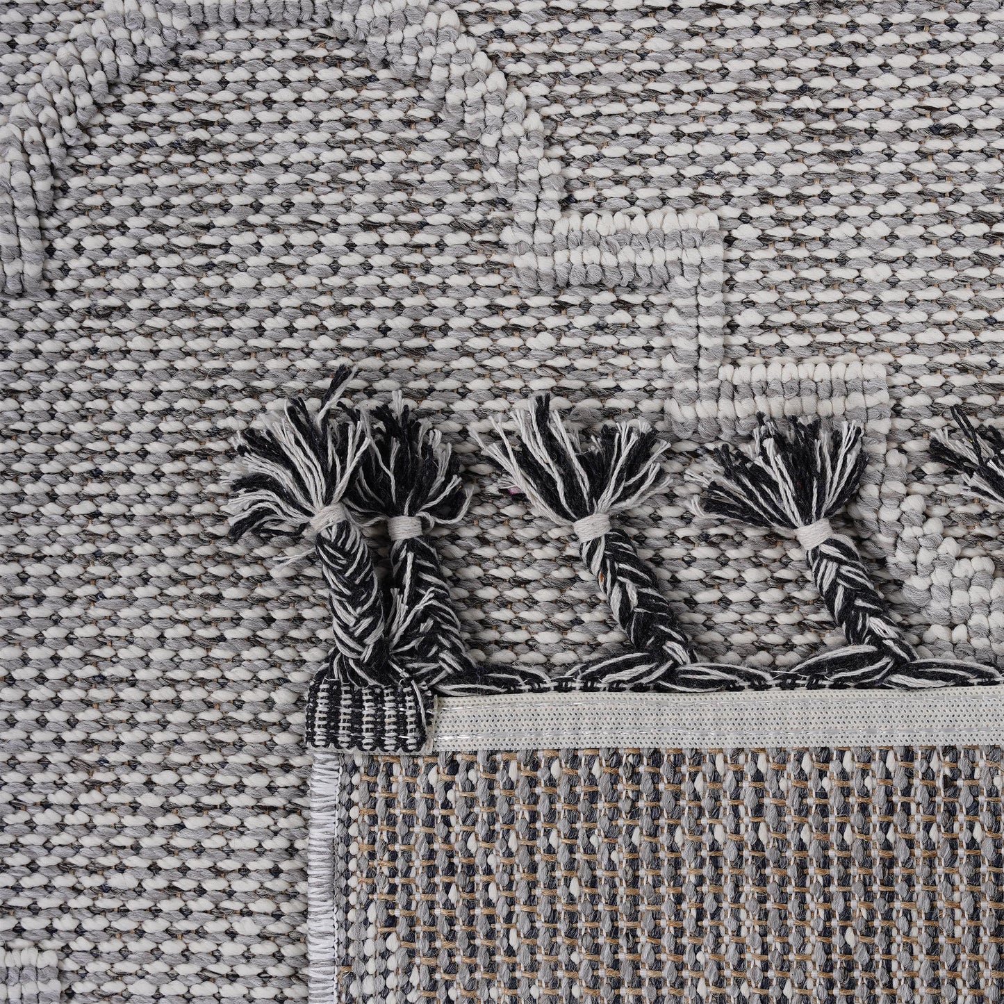 Closeup texture of a grey and white woven rug with black and white tassels