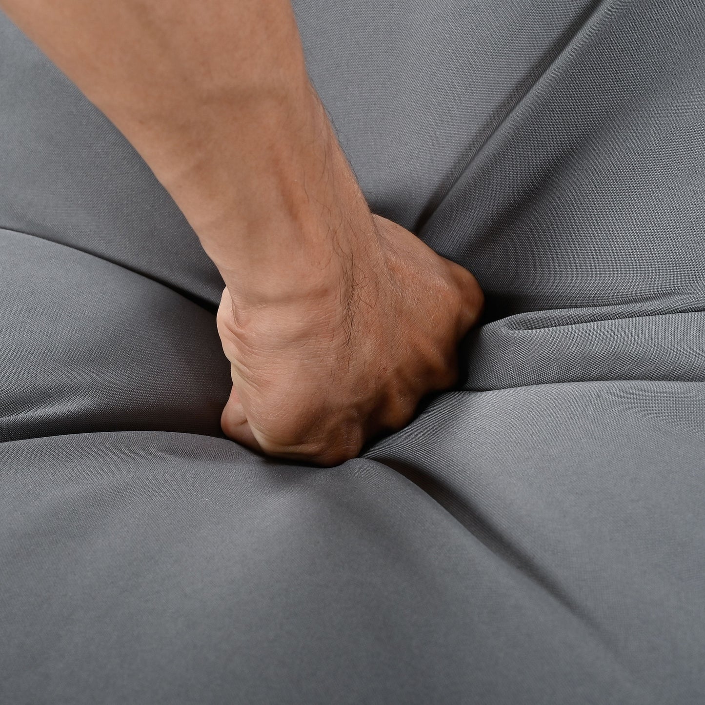 Hand pressing into a flexible gray fabric cushion demonstrating plush comfort