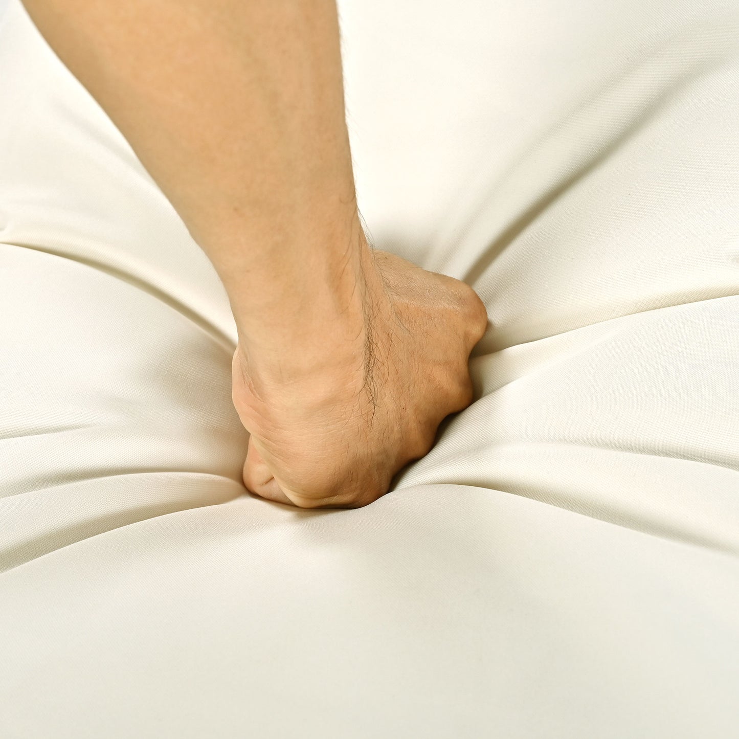 Closeup of a hand pressing into a plush ivory fabric highlighting comfort