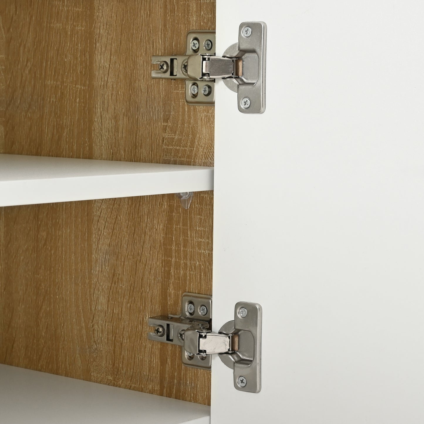 Closeup of brushed nickel cabinet hinges on white door and wood grain interior