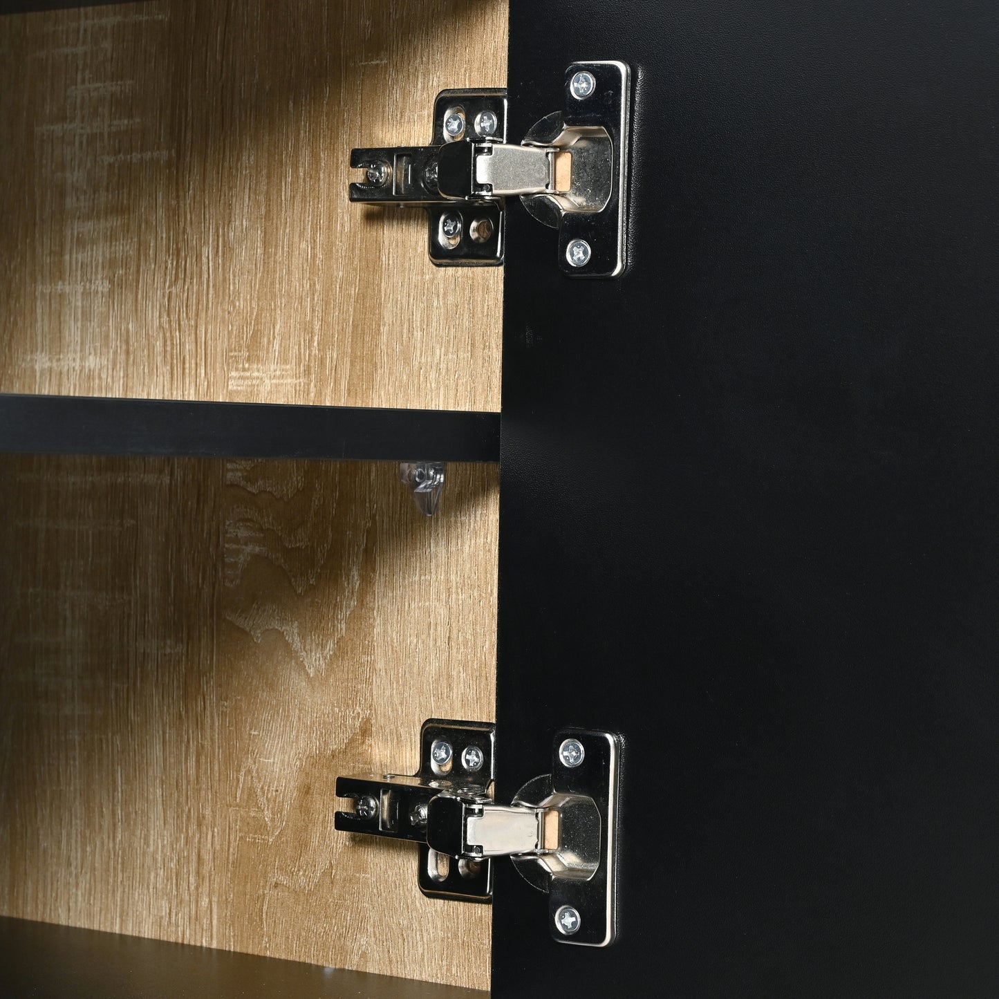 Closeup of two silver cabinet door hinges on black and wood grain panels