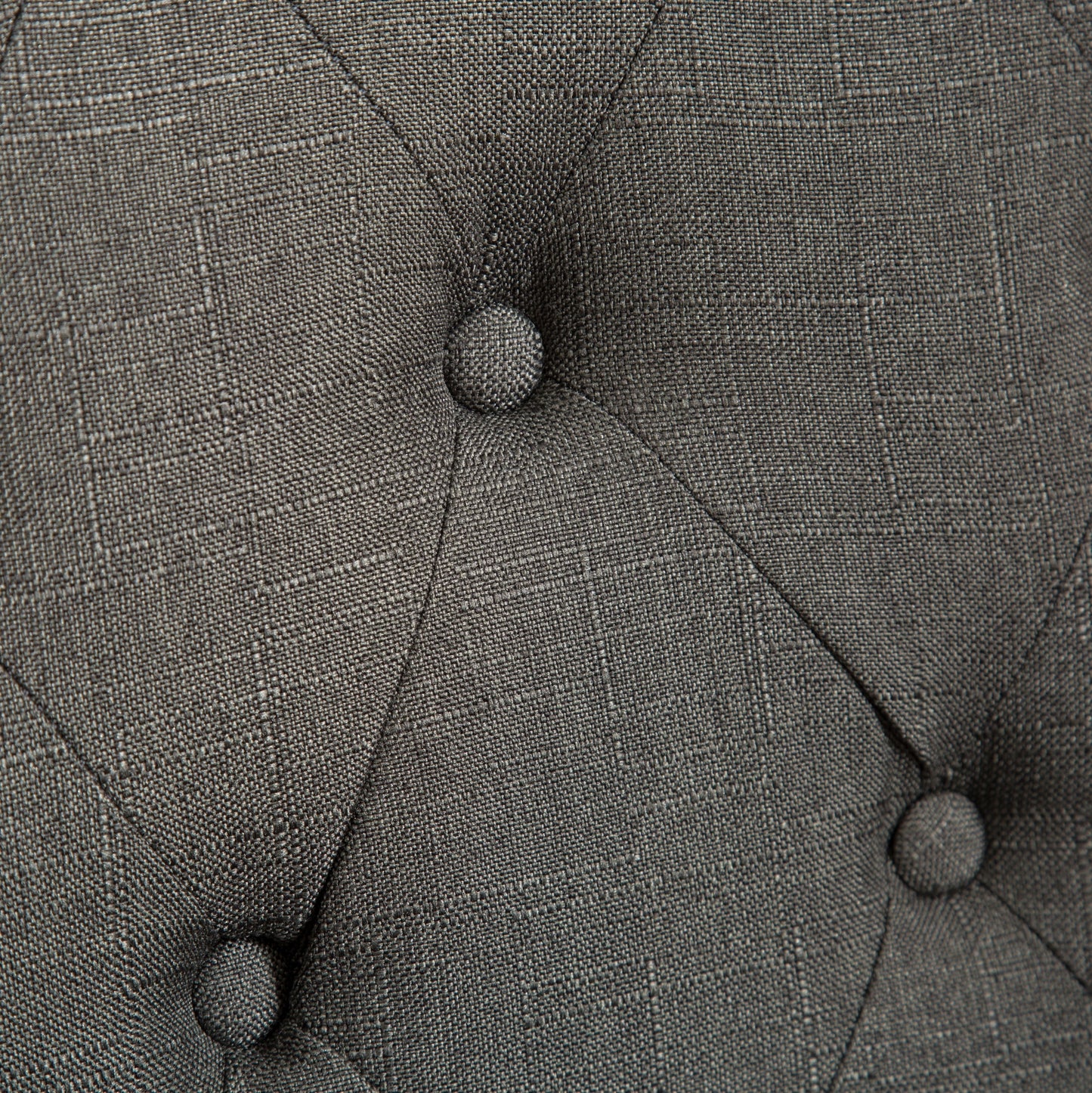 Closeup of tufted dark grey fabric with diamond pattern stitching showcasing textile texture