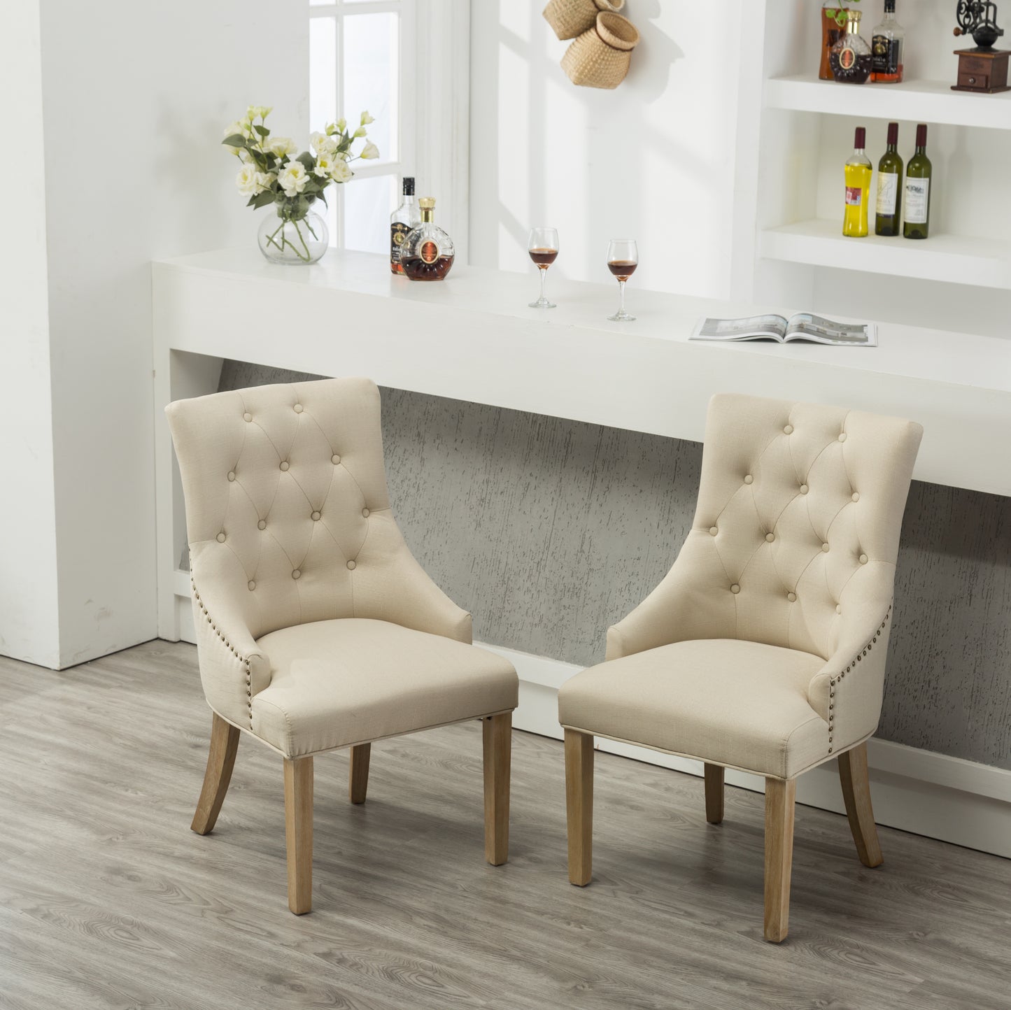 Two beige linen dining chairs with button tufting and nailhead trim