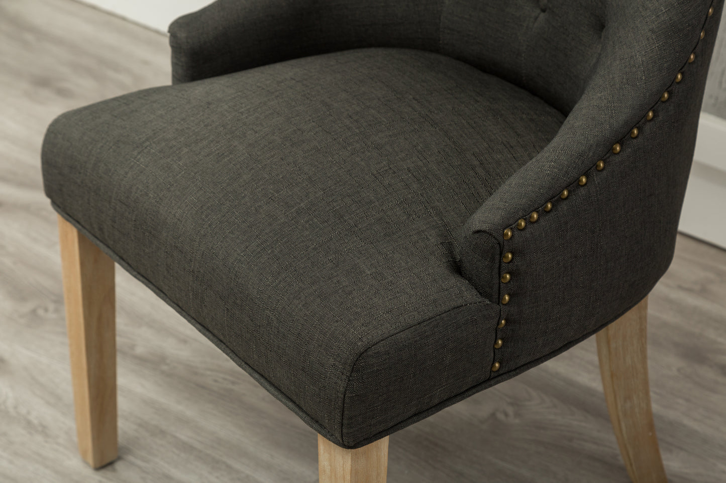 Dark grey upholstered chair with brass nailhead trim and light wood legs