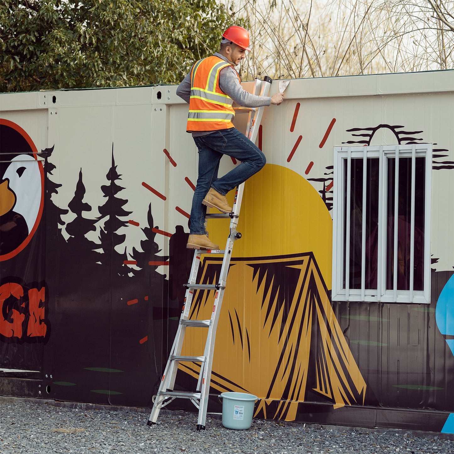 Worker in hard hat and vest on a multipurpose aluminum ladder securing a package