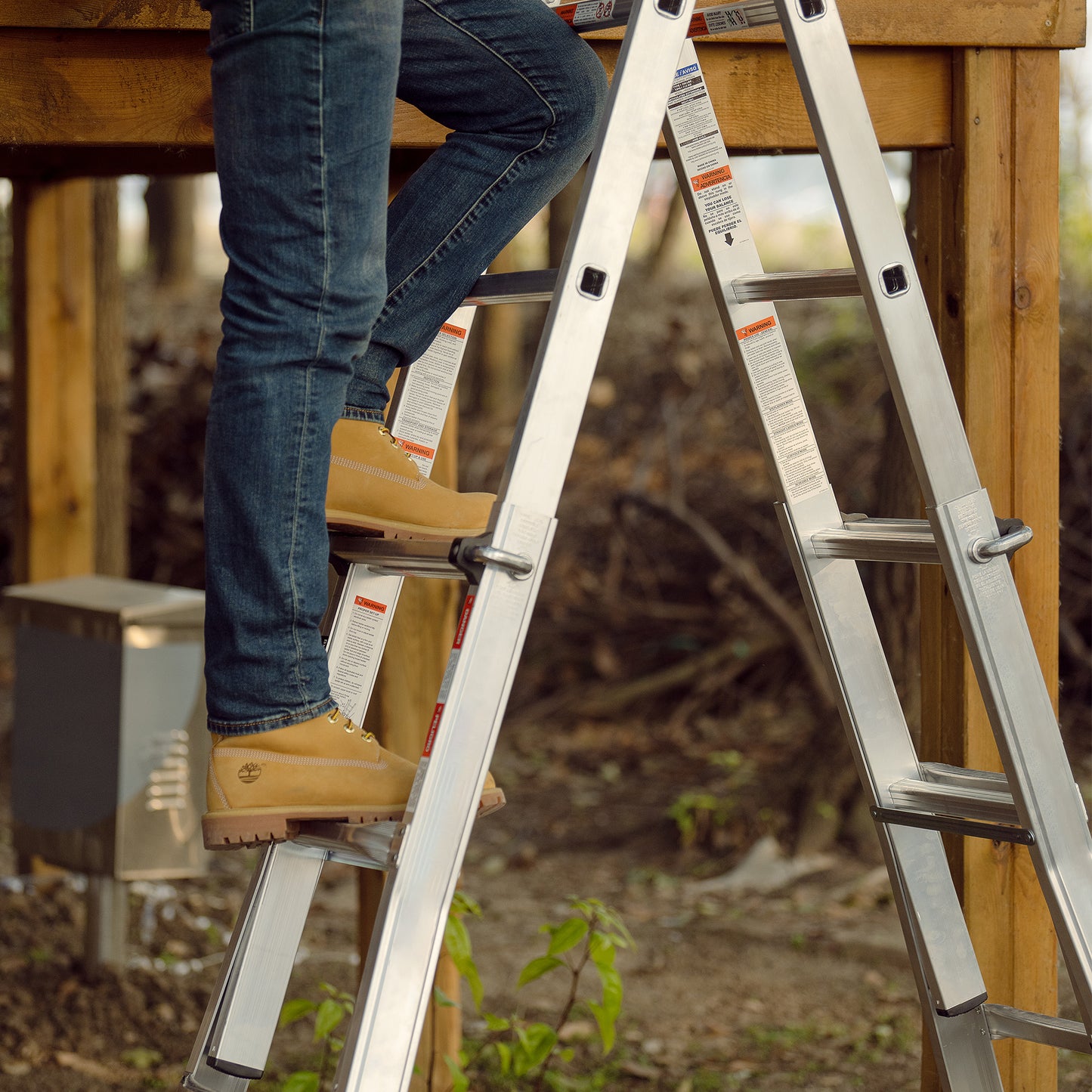 Person in work boots climbing a durable aluminum multipurpose ladder with safety warnings