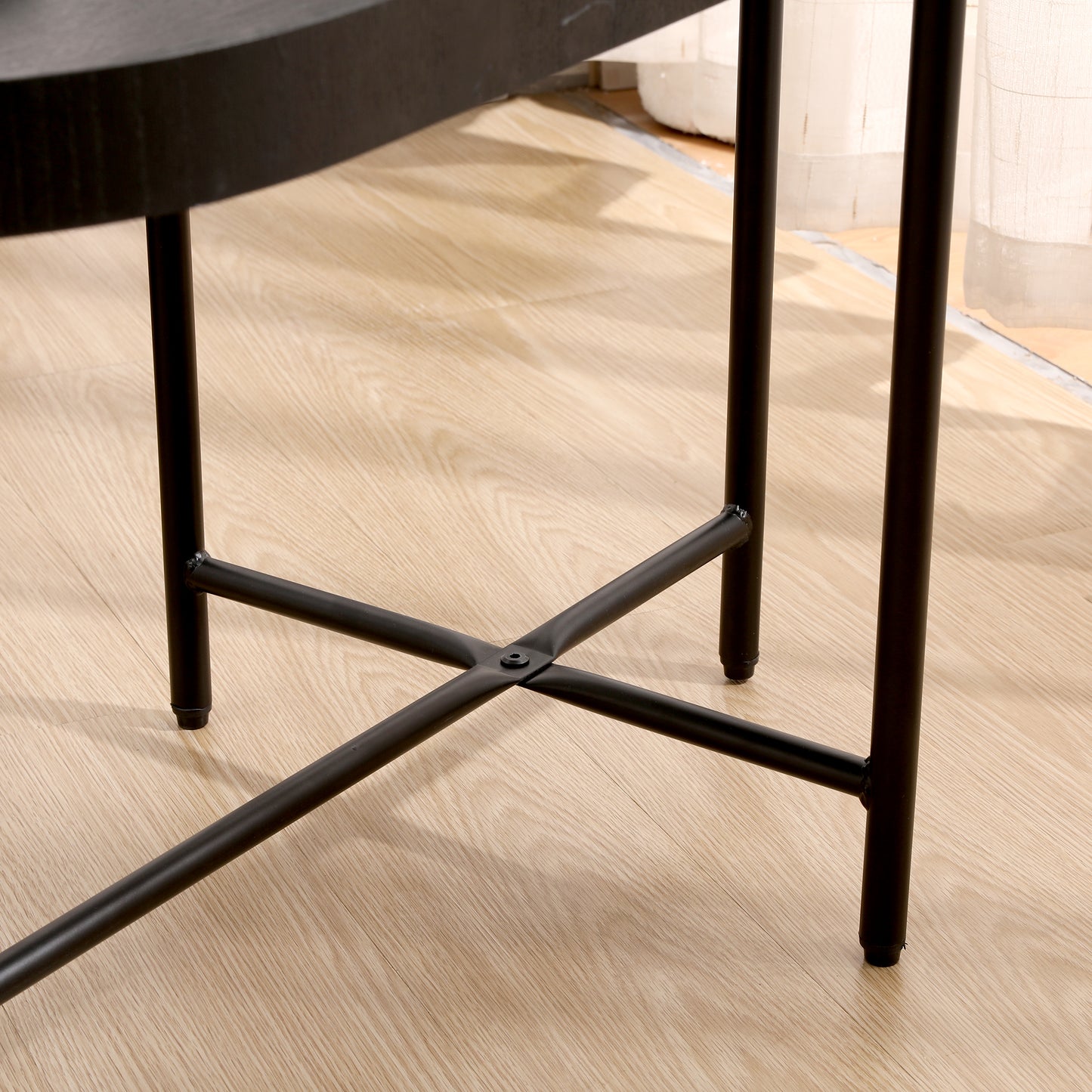 Closeup of a black metal coffee table base with a crossshaped support on a light wood floor