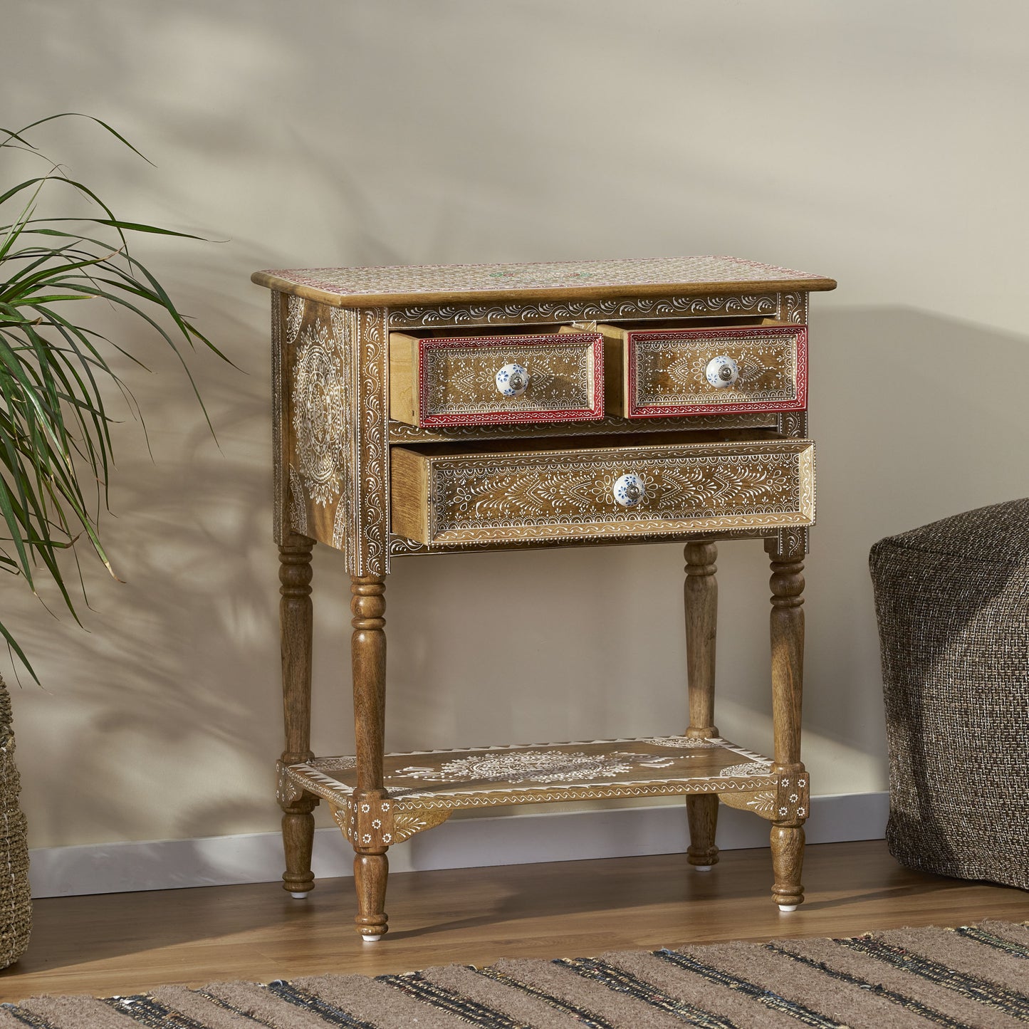 Wooden accent table with ornate white carvings and three drawers with ceramic knobs