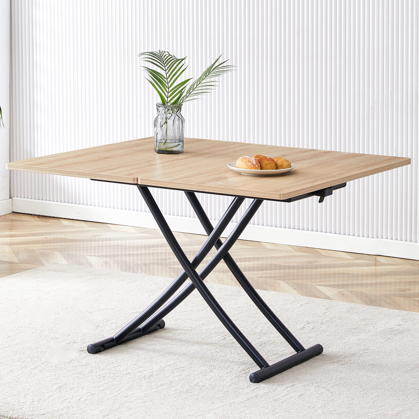 Light oak lift top coffee table with black scissor legs and decorative greenery