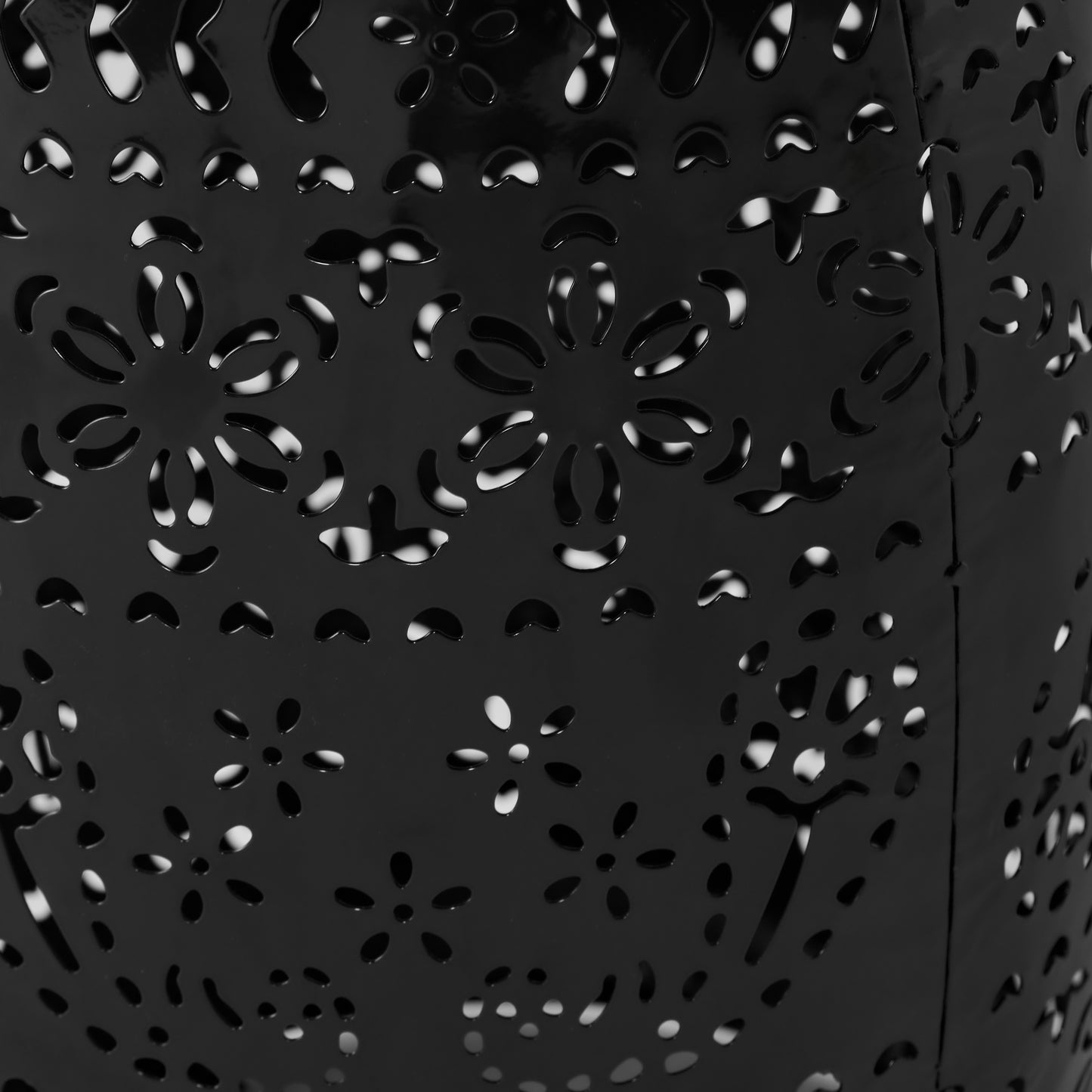Closeup of a black metal lantern with intricate floral cutouts casting patterned light