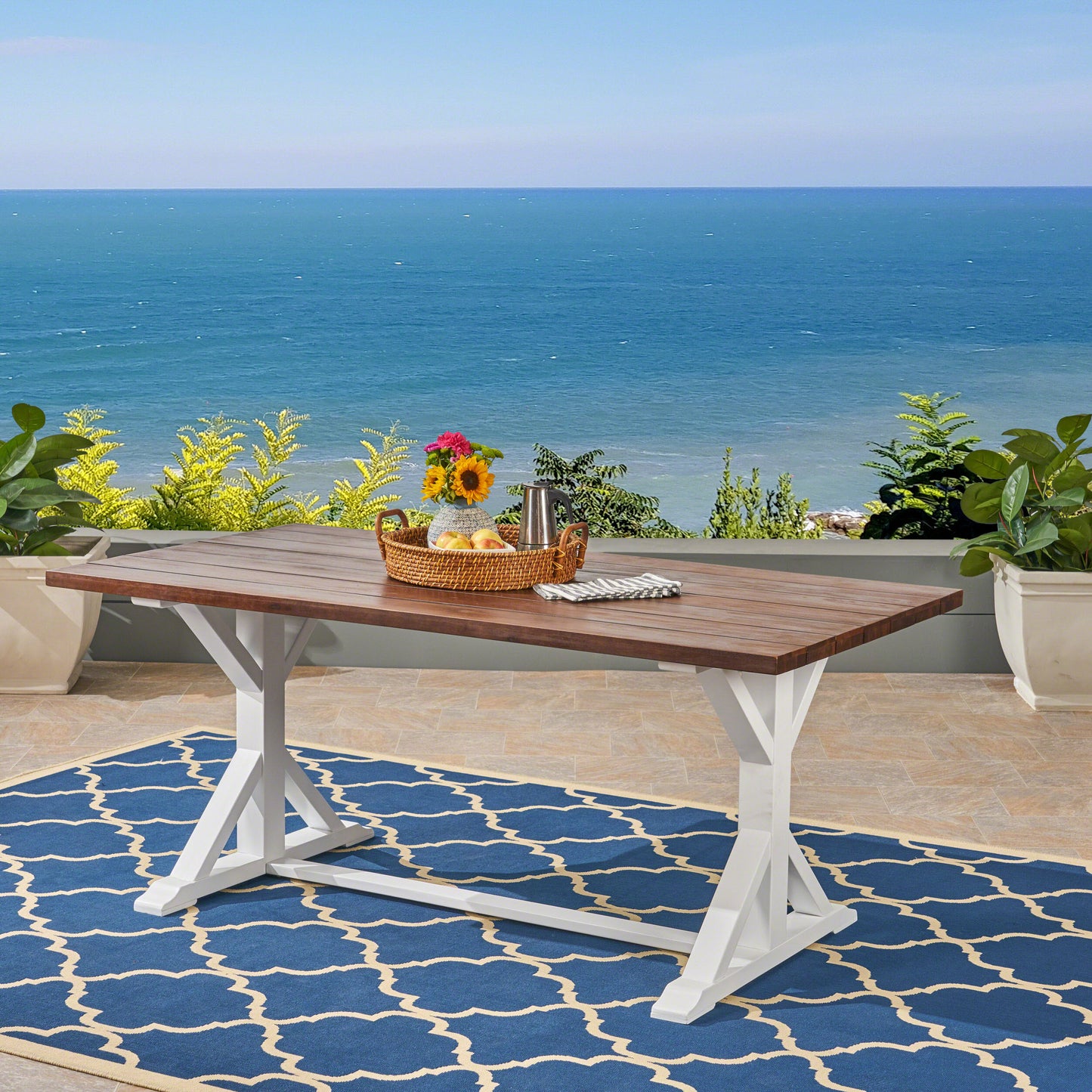 Rectangular wooden picnic table with white trestle legs set on a blue outdoor rug