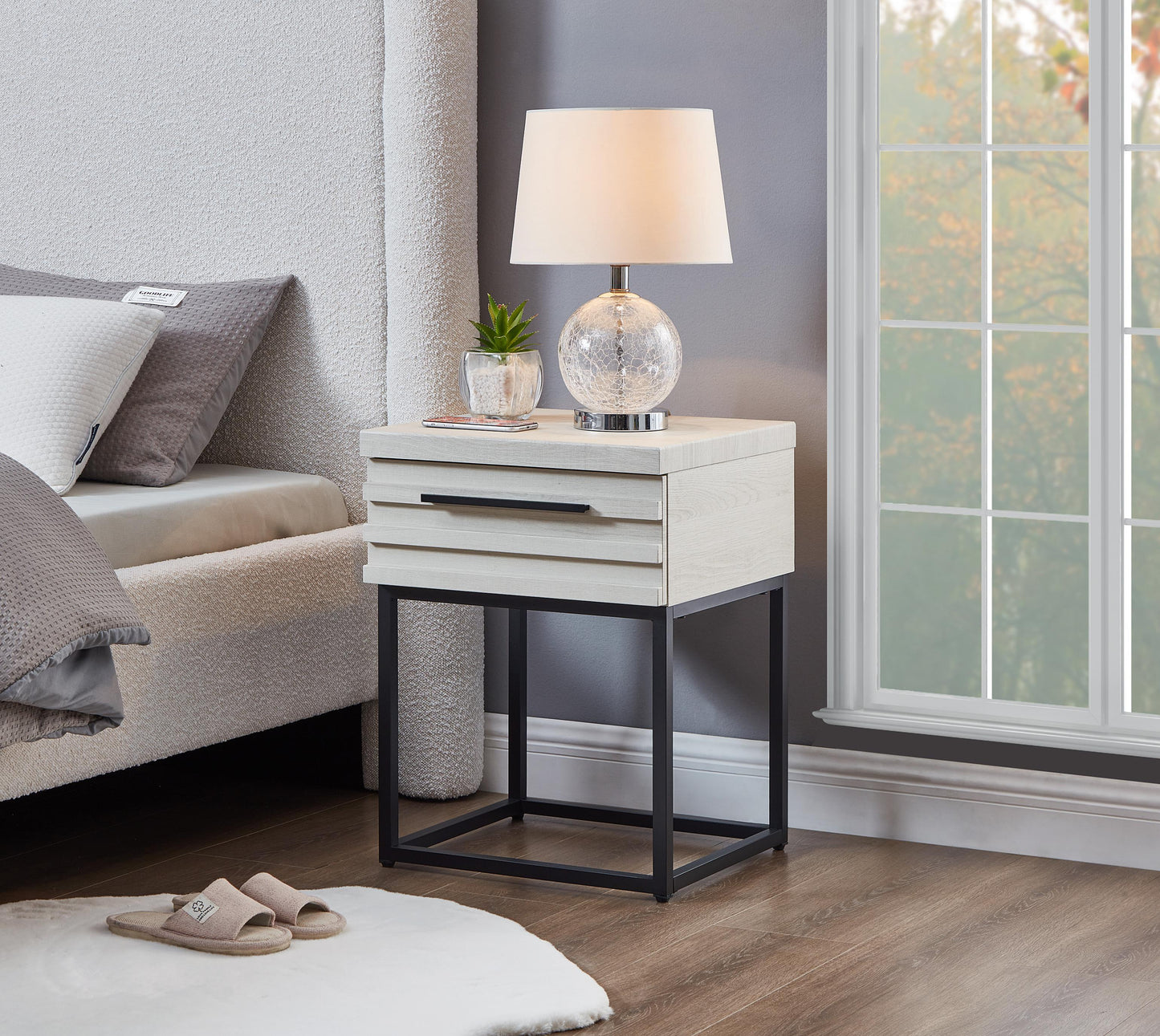Whitewashed wood nightstand with black metal frame and two drawers next to bed