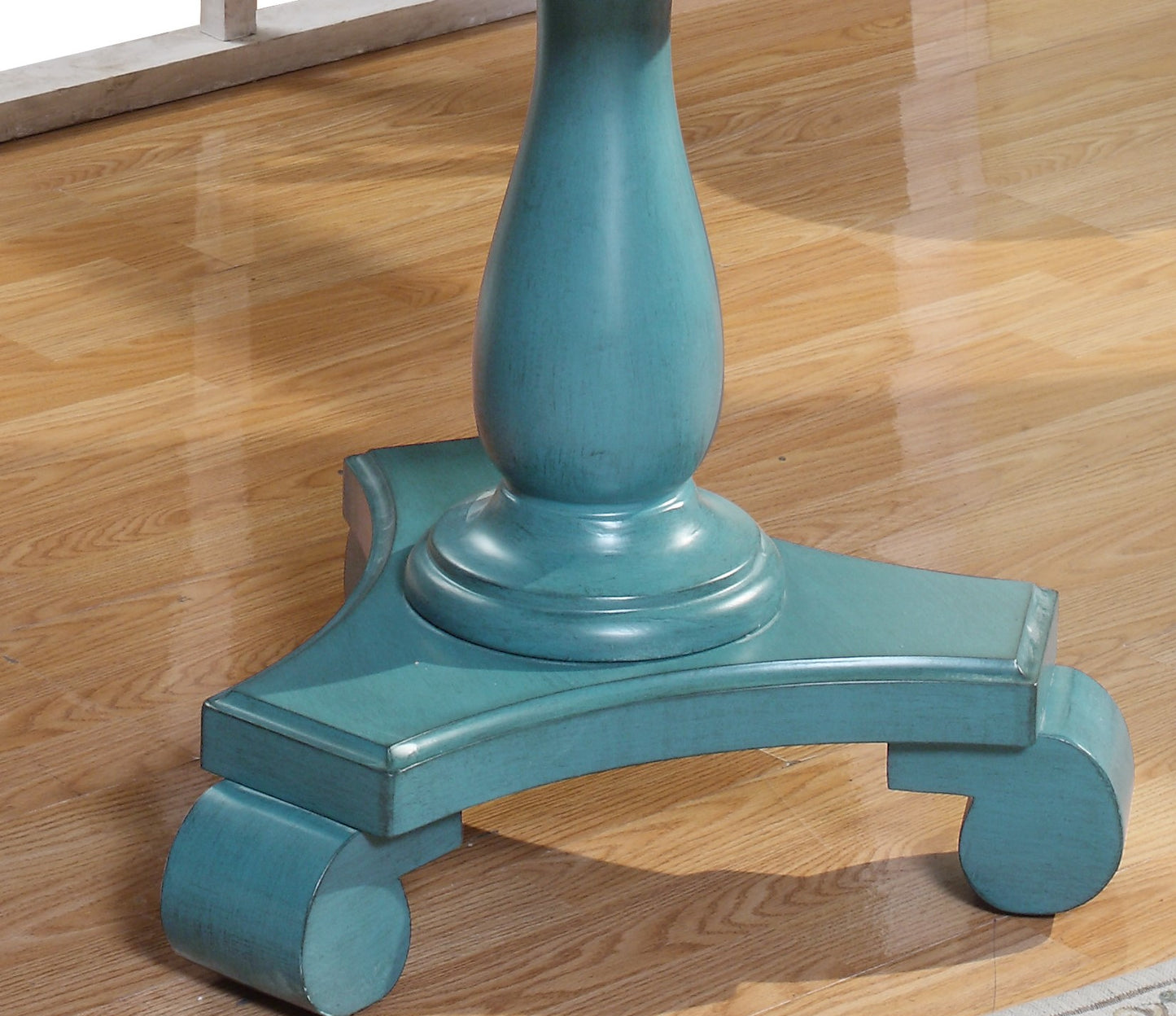Antique teal pedestal base with carved wooden feet on a polished floor
