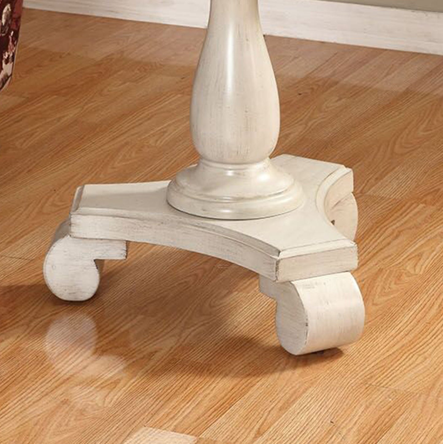 Distressed white pedestal table base with scroll feet on wood floor