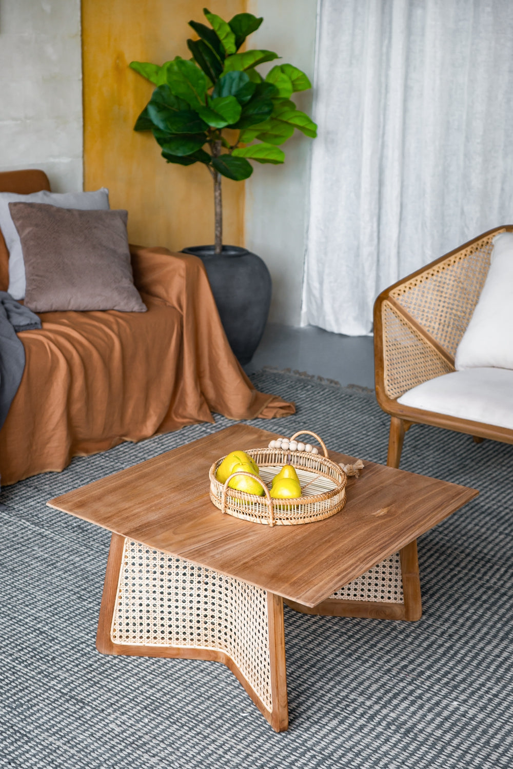 Natural wood coffee table with woven cane accents and pears in a rattan tray