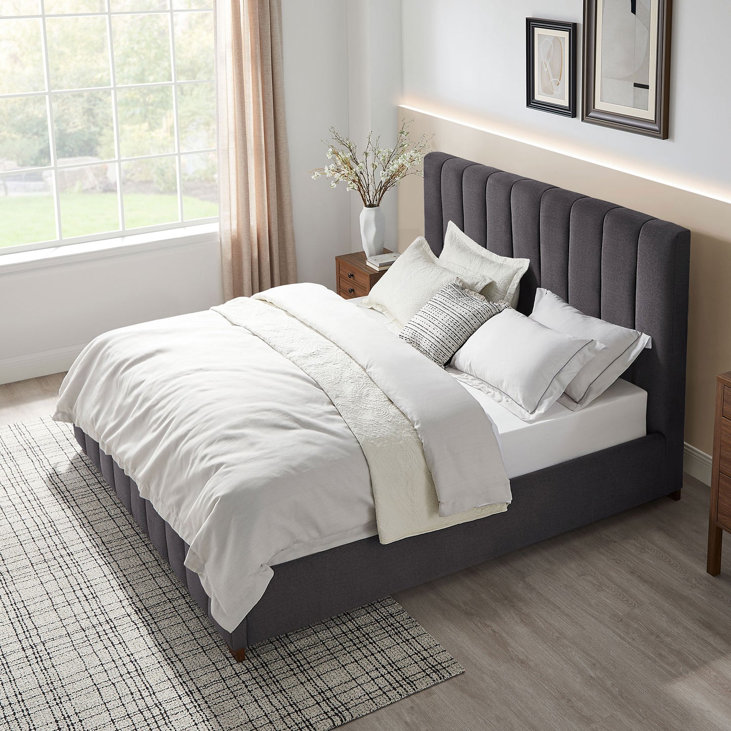 Dark gray upholstered platform bed with vertical channel tufting and white linens