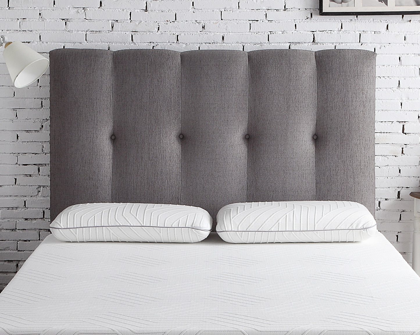 Tufted charcoal grey fabric headboard with channel stitching paired with two white geometric patterned pillows
