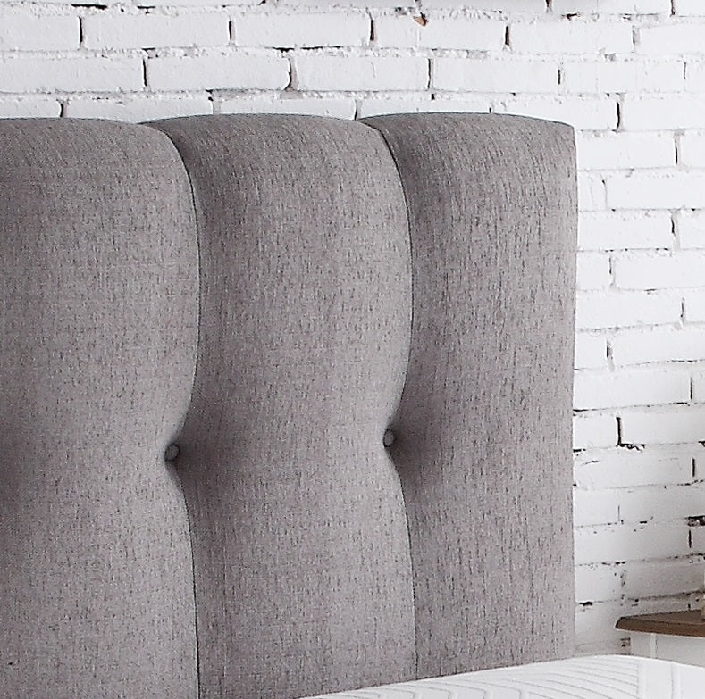 Upholstered grey headboard with button tufting and vertical channel stitching