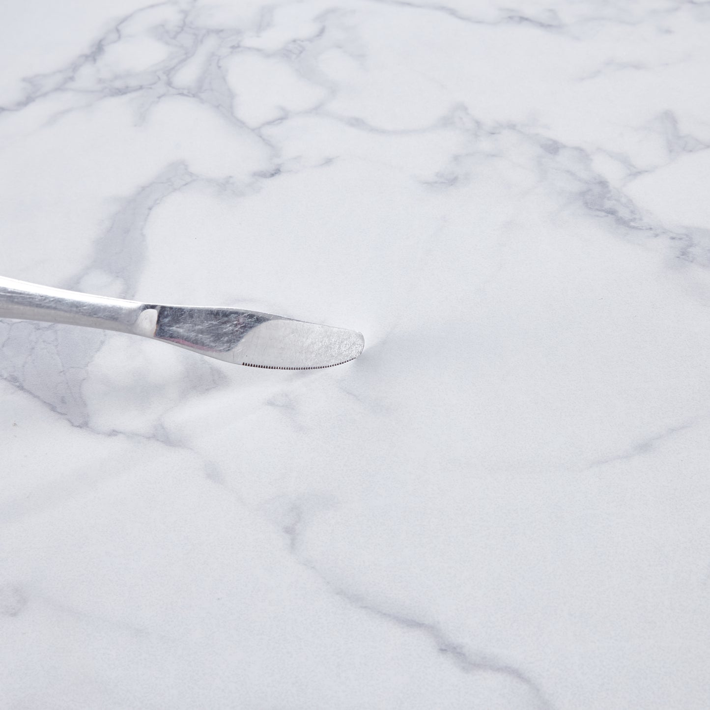 Polished stainless steel butter knife with serrated edge on white marble background
