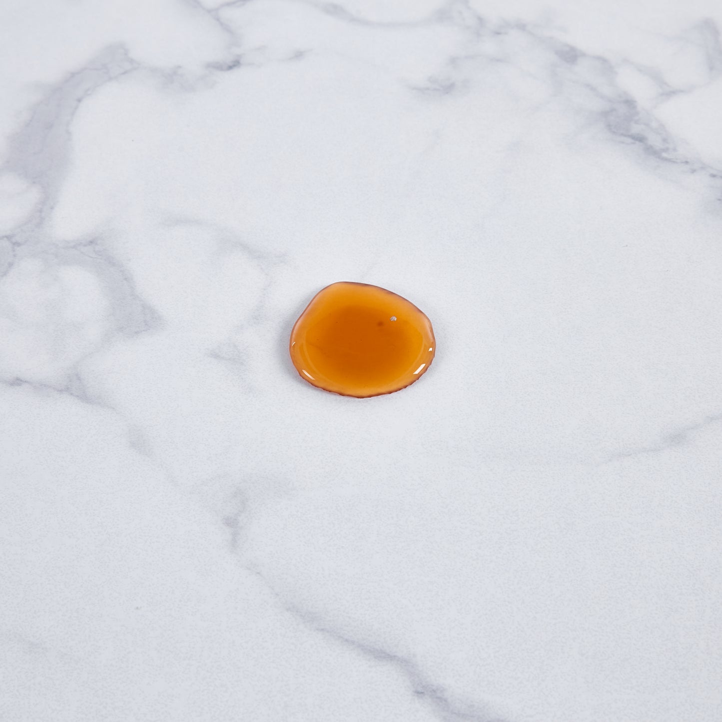 Amber colored facial serum drop on a white marble background