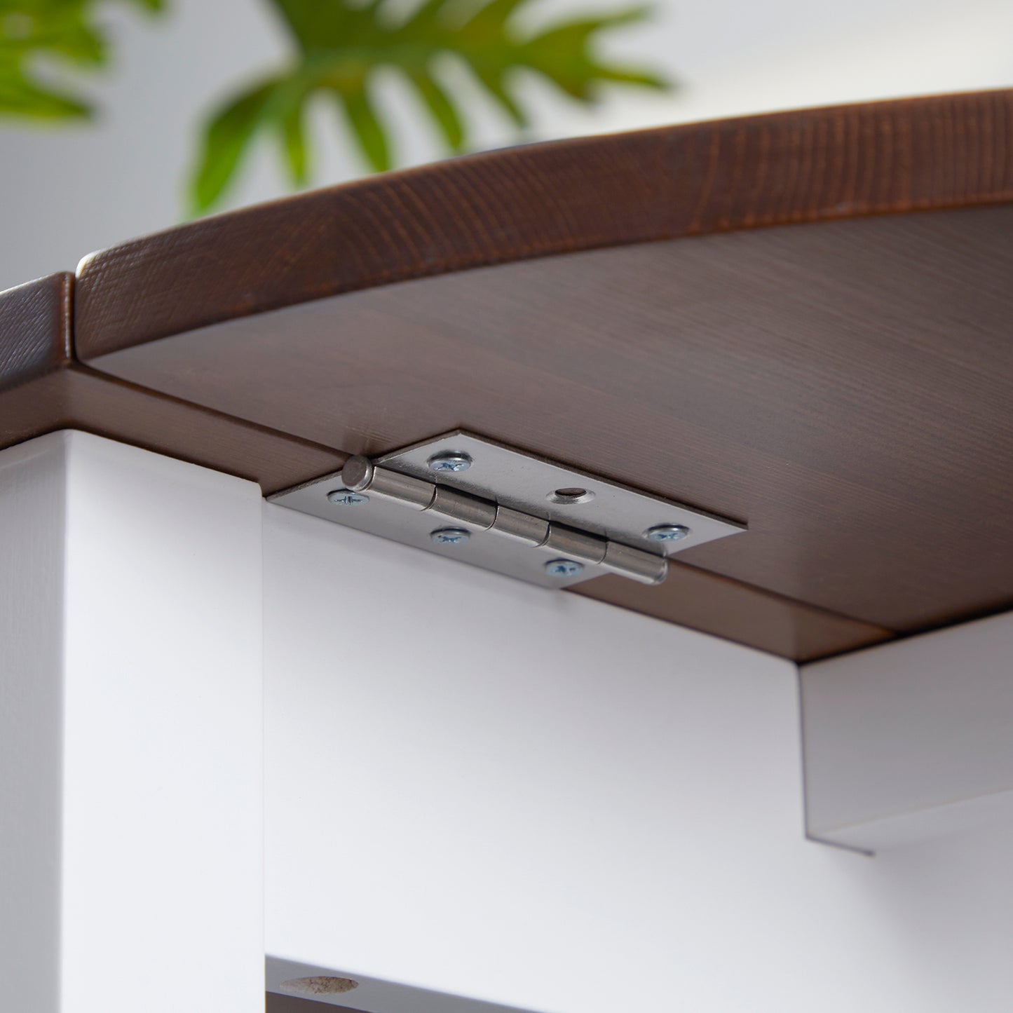 Closeup of a brushed nickel hinge on a dark wood dropleaf table