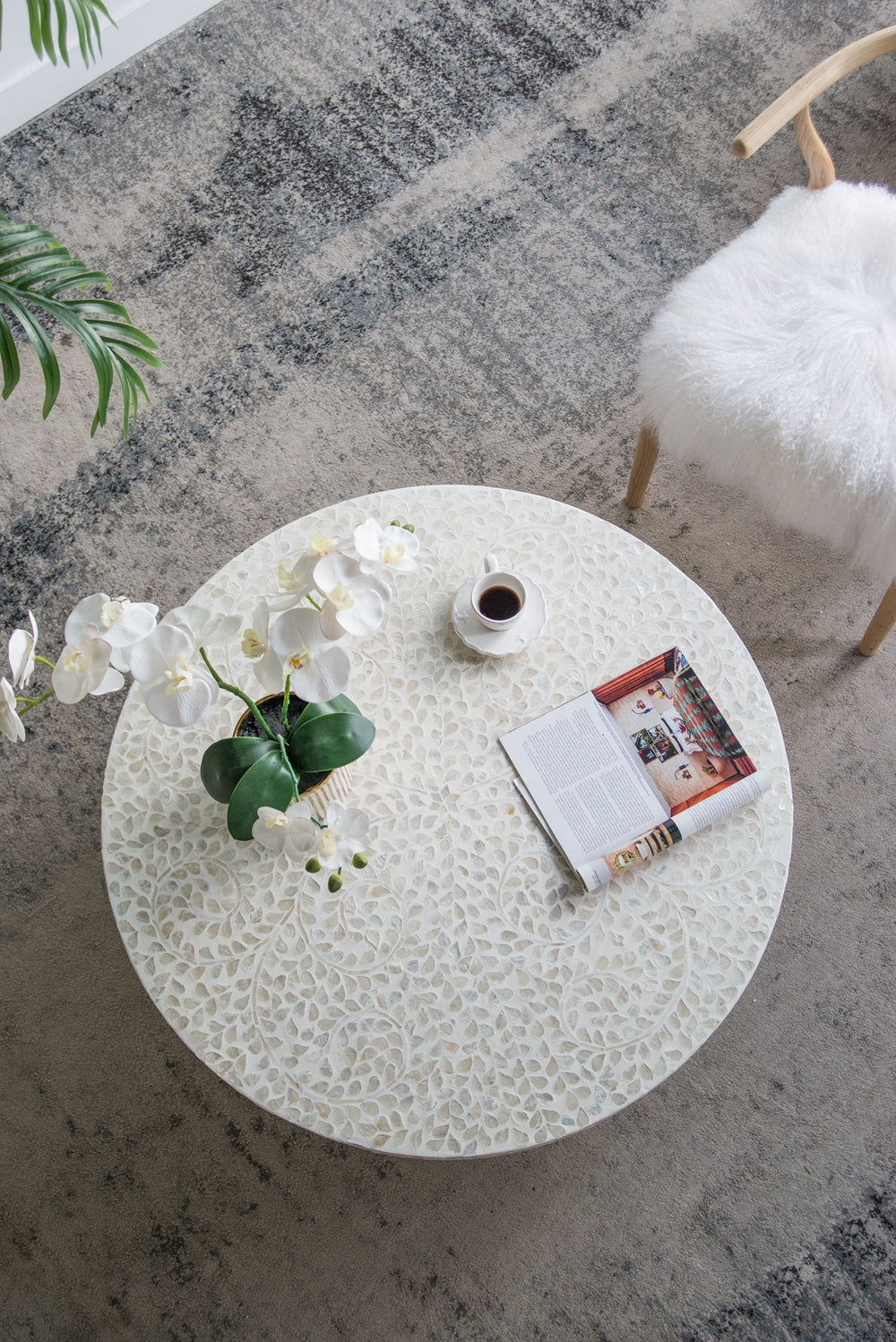 White inlaid coffee table with intricate leaf pattern a cup of coffee and orchids
