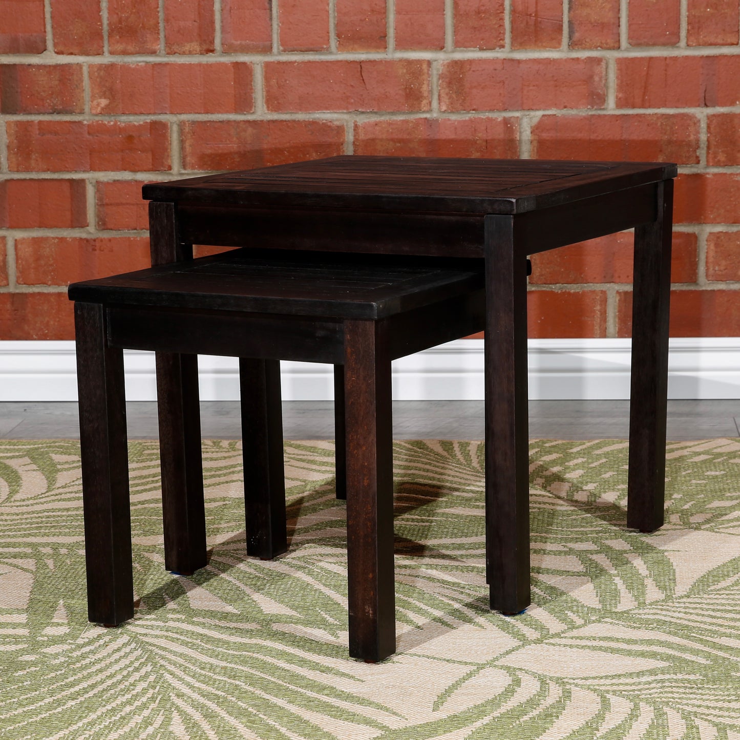 Dark brown wooden nesting tables with slatted tops placed on a tropical leaf print rug