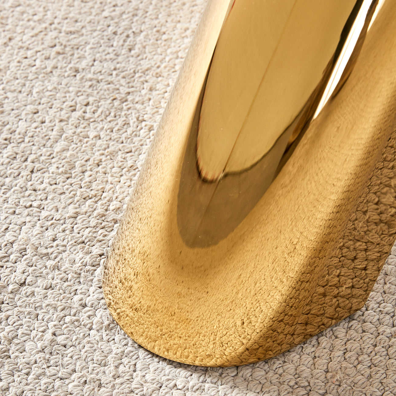 Polished gold metallic furniture leg resting on a textured beige rug