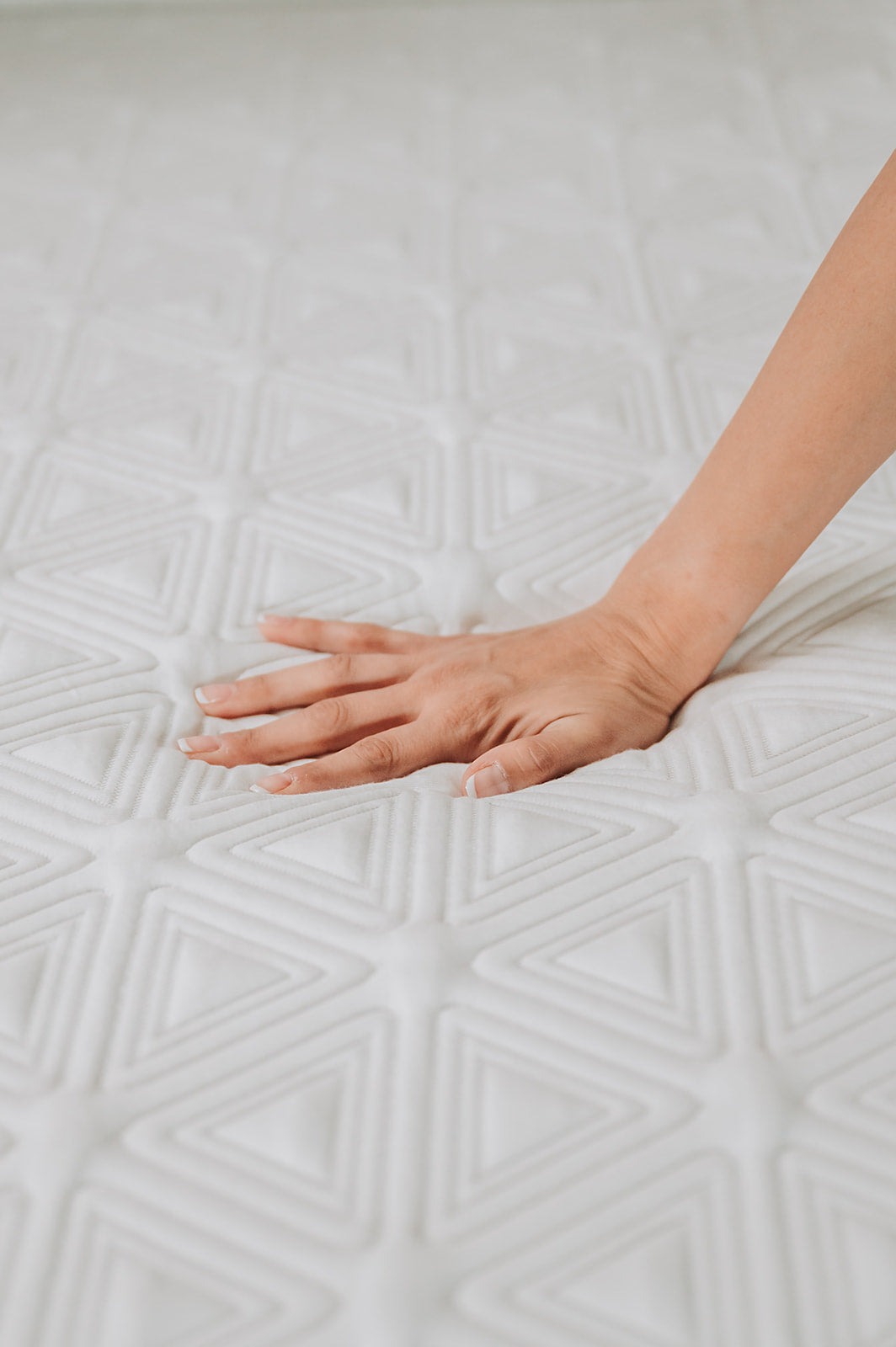 Hand pressing into white quilted mattress fabric with geometric triangle pattern