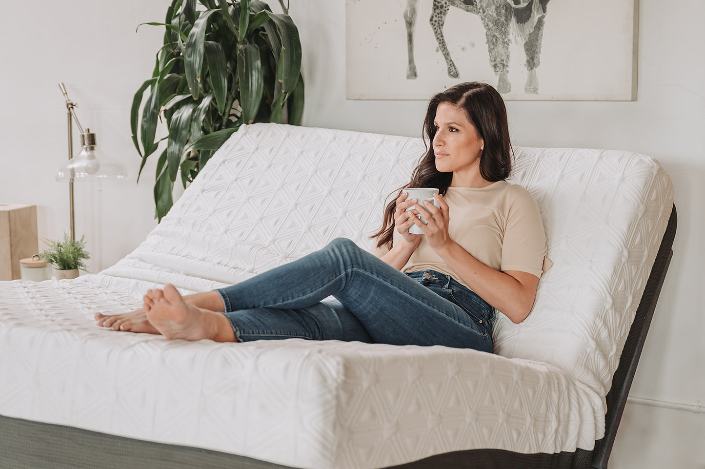 Adjustable bed frame with white quilted mattress woman holding mug and relaxing