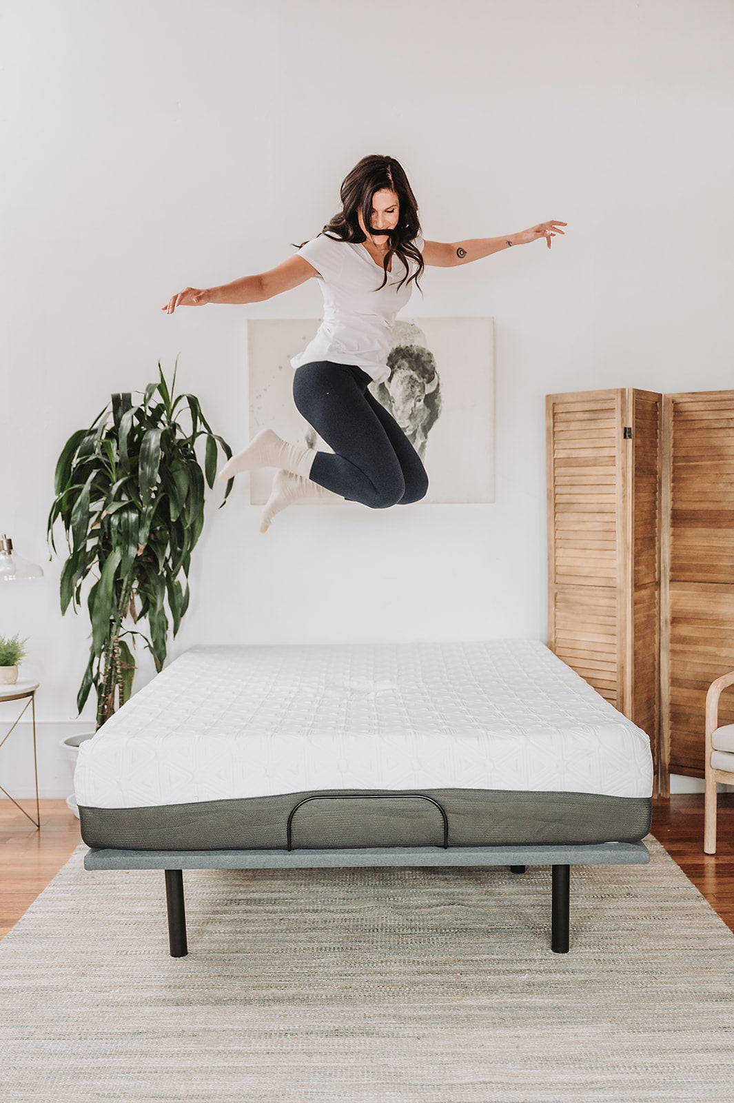 Woman happily jumping on a white quilted memory foam mattress on a gray adjustable base