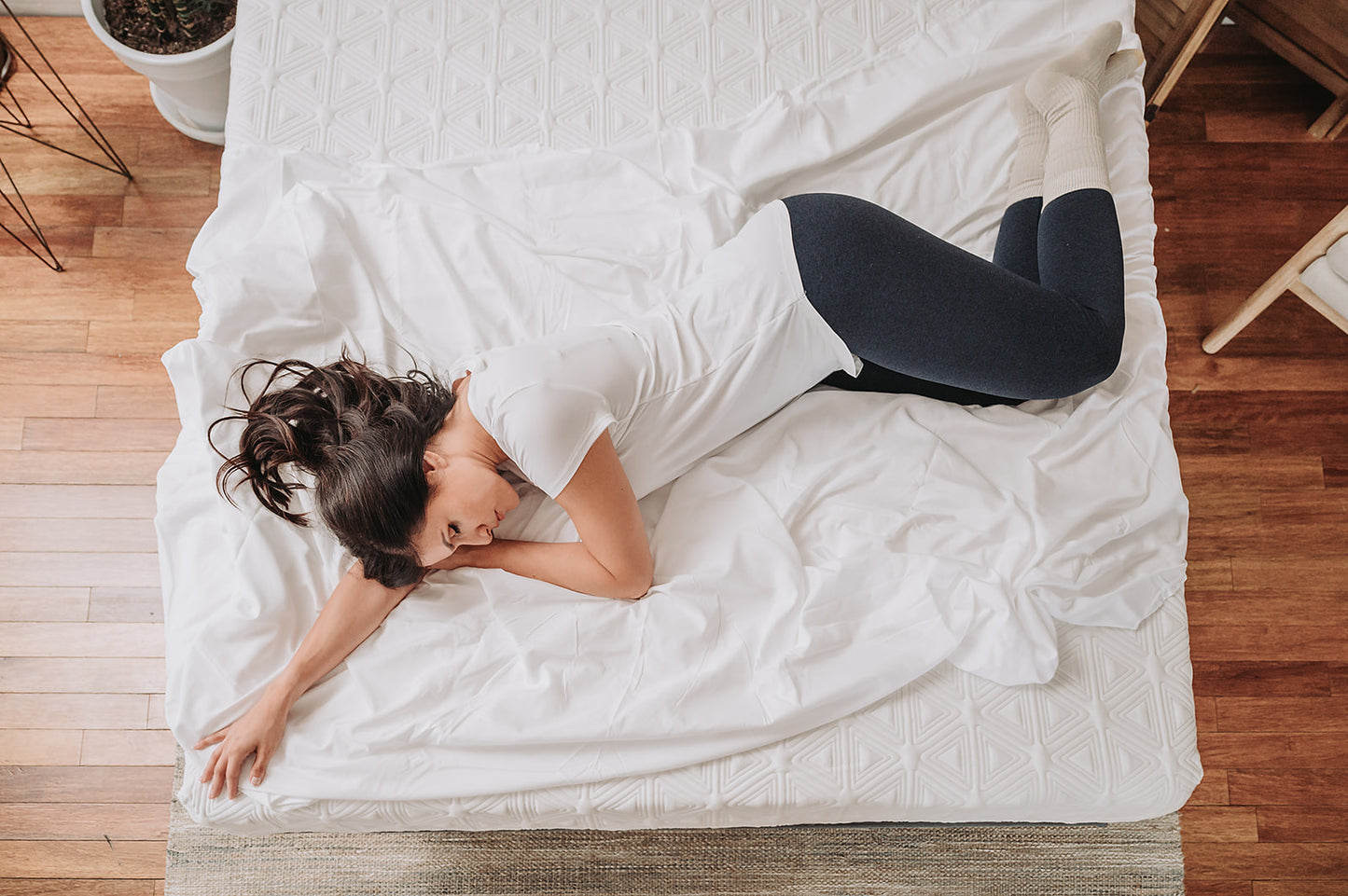 Woman in white tshirt and dark blue leggings relaxing on a white crinkled duvet premium bedding