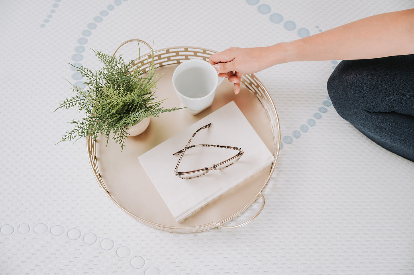Gold serving tray with eyeglasses plant and mug on a mattress