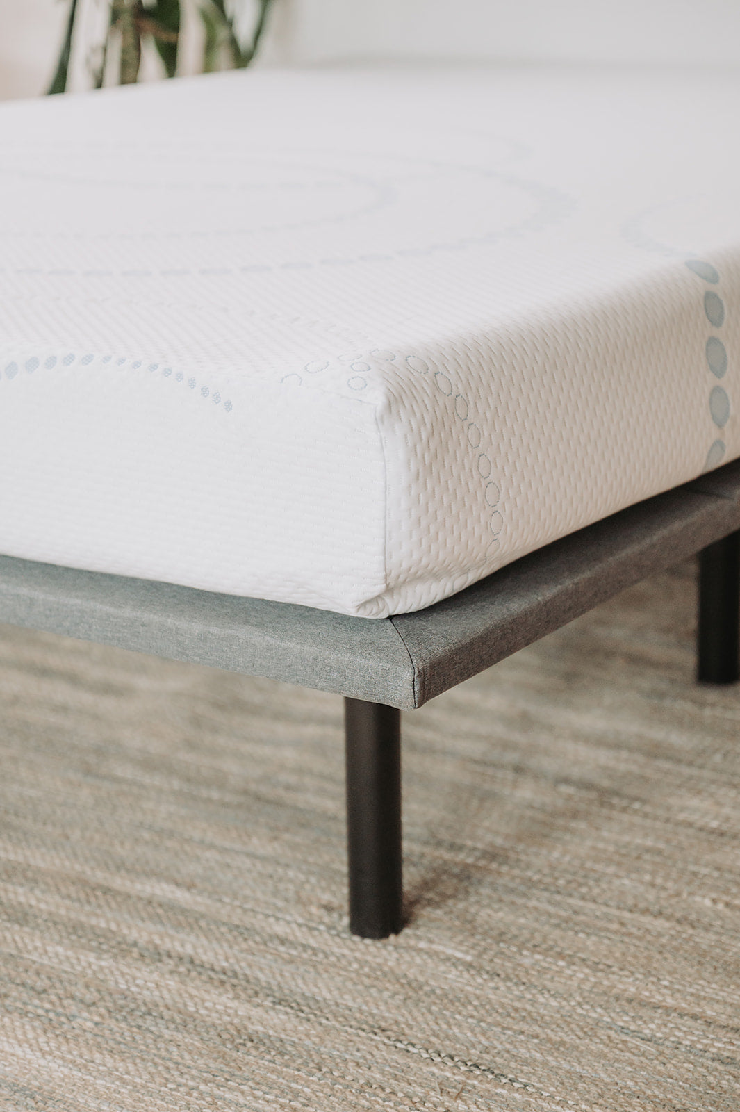 Closeup of a white mattress with subtle blue circular patterns on a gray bed frame with black legs