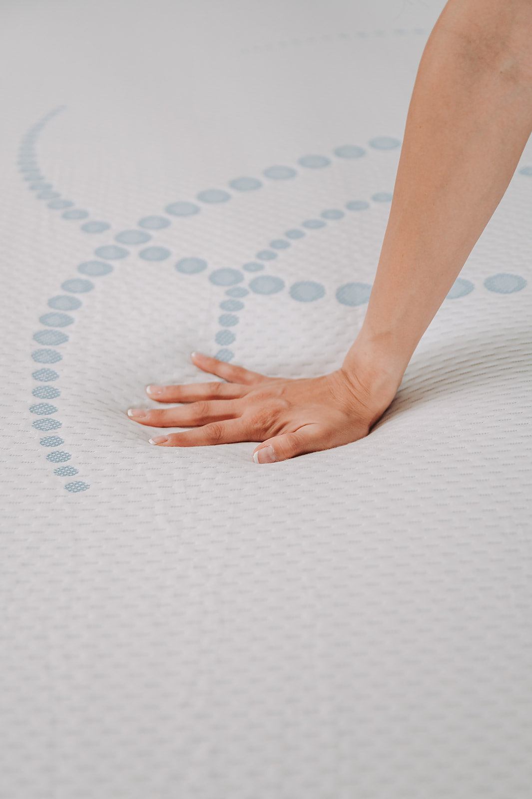 Closeup of a hand pressing into a white memory foam mattress with a subtle blue geometric pattern