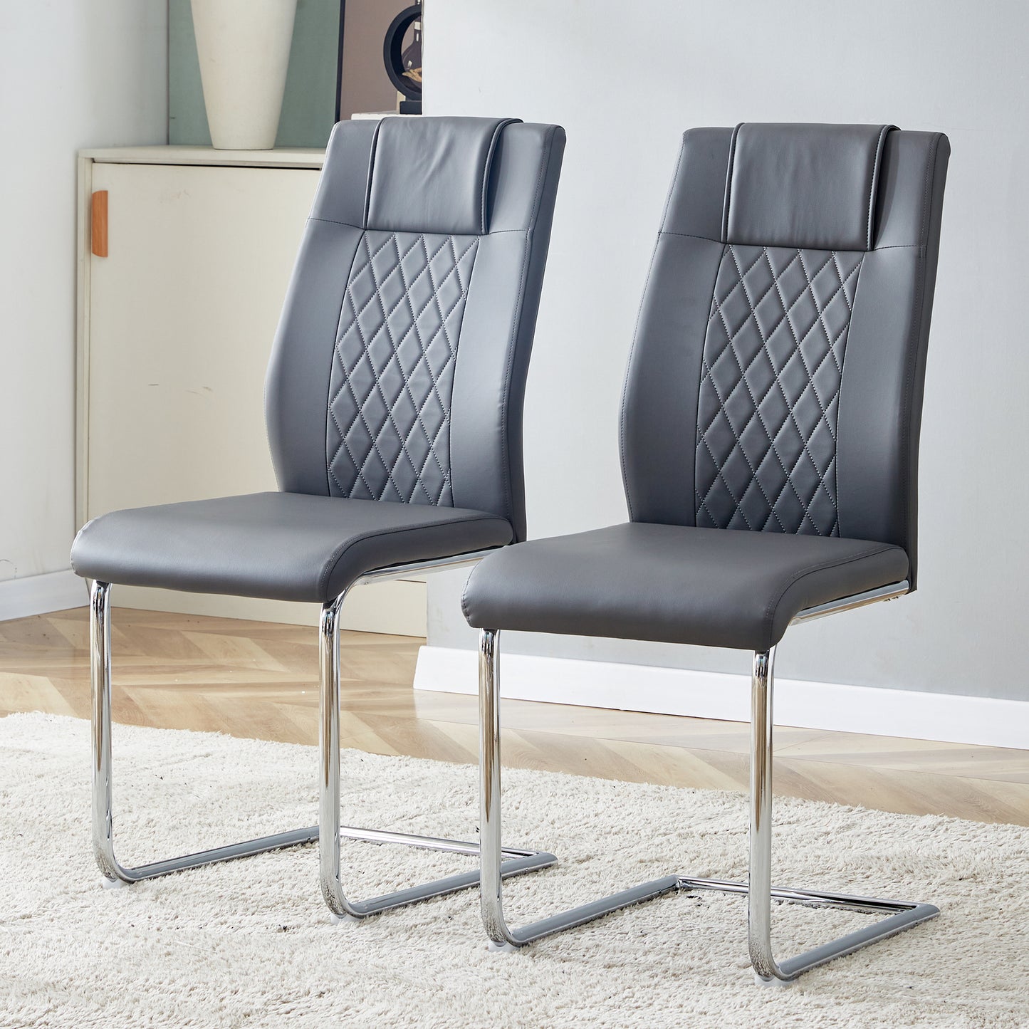 Two grey faux leather dining chairs with diamond stitching and chrome legs