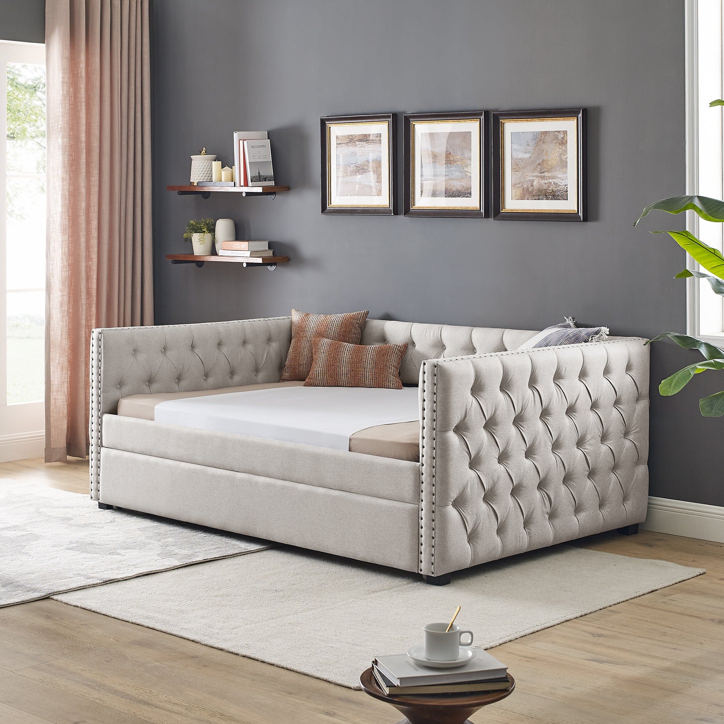 Tufted beige fabric daybed with silver nailhead trim and bolster pillows