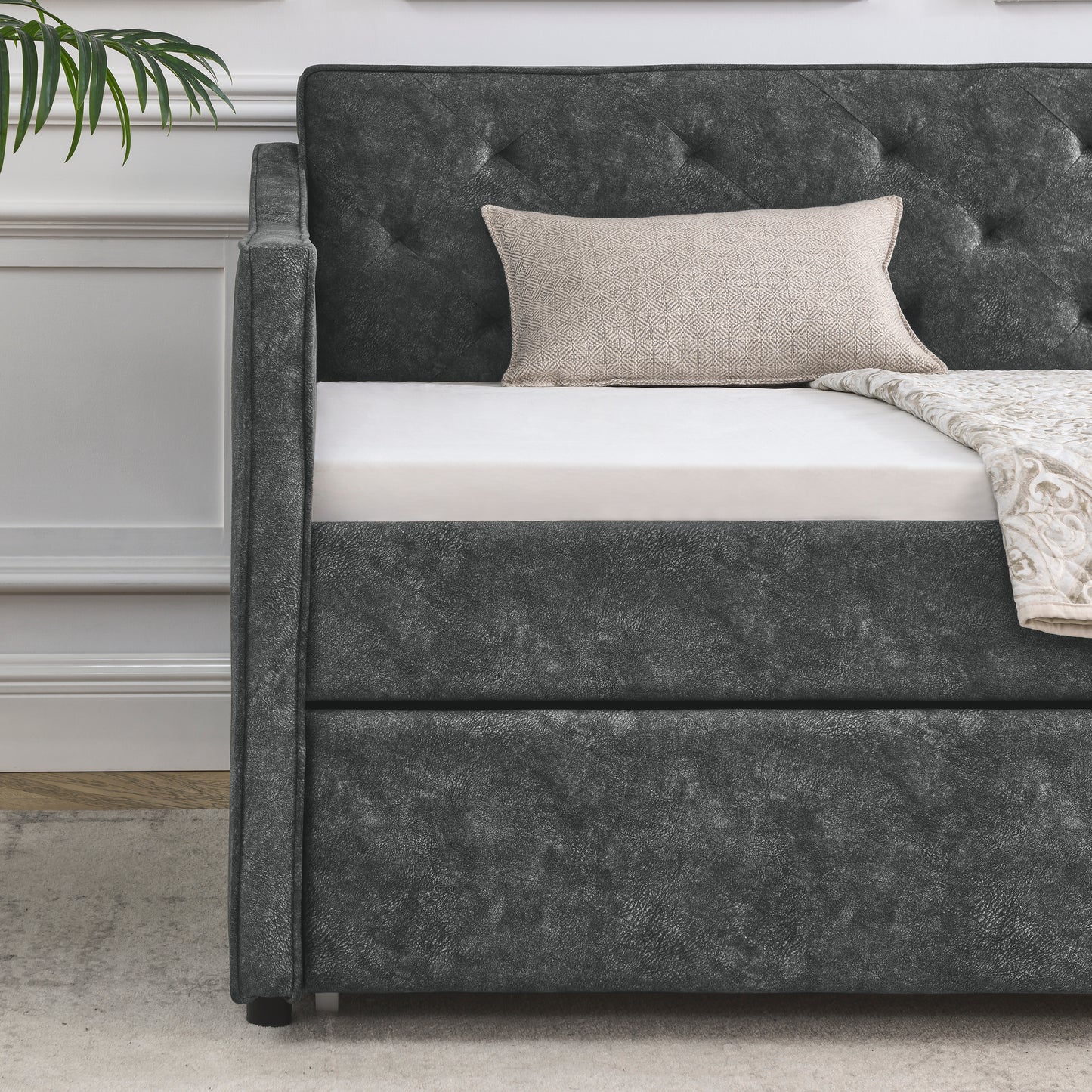 Dark gray faux leather tufted daybed with a cream patterned pillow