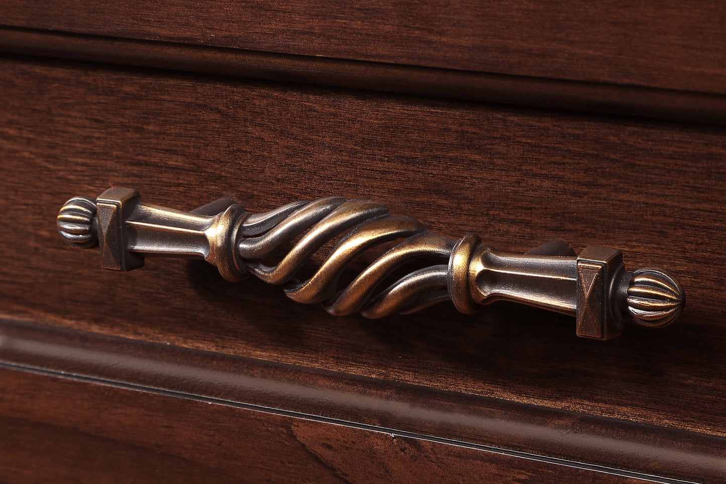 Antique brass drawer pull with ornate twisted design on dark wood