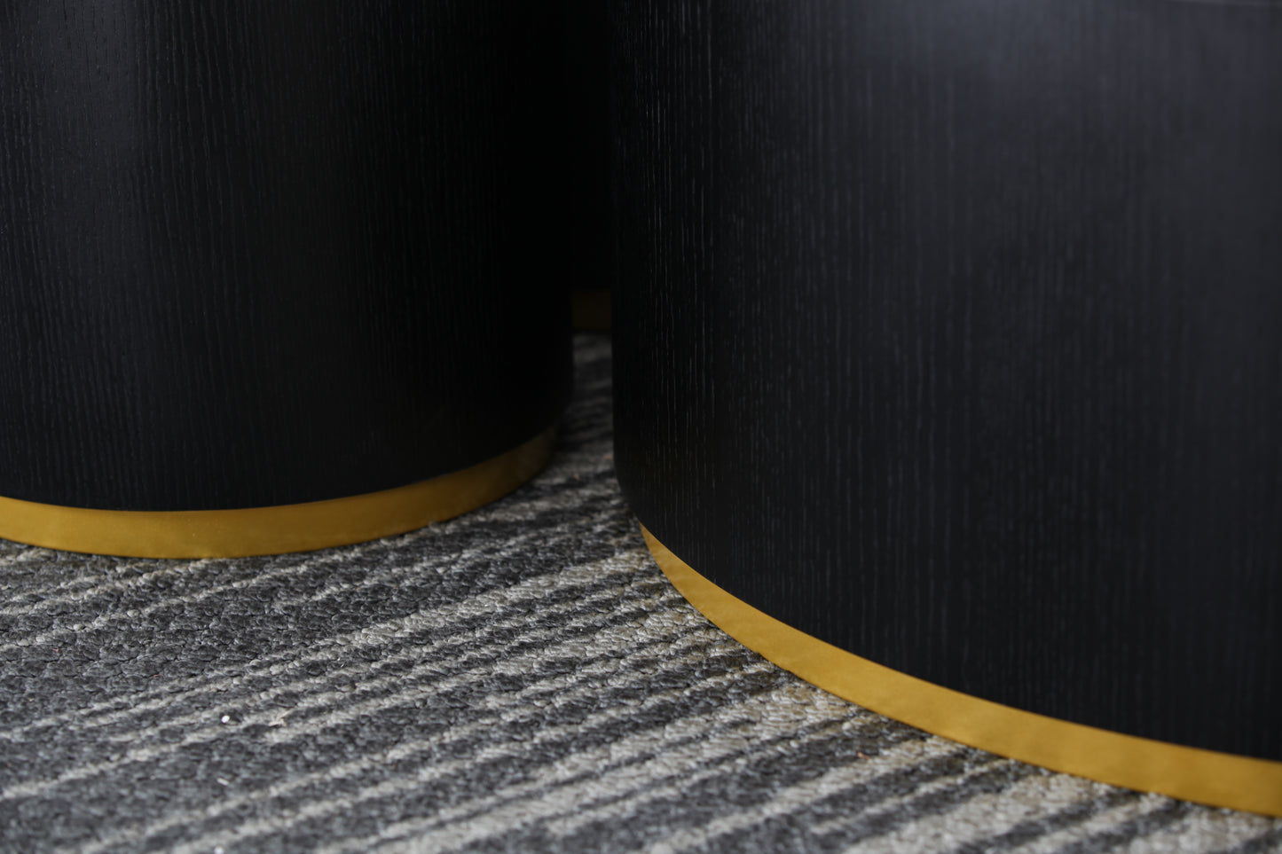 Closeup of a black cylindrical side table with a brushed gold base on a textured rug