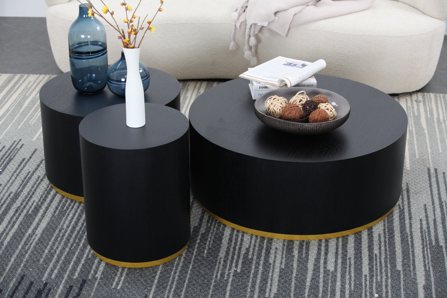 Three modern black cylindrical coffee tables with gold bases arranged on a striped rug