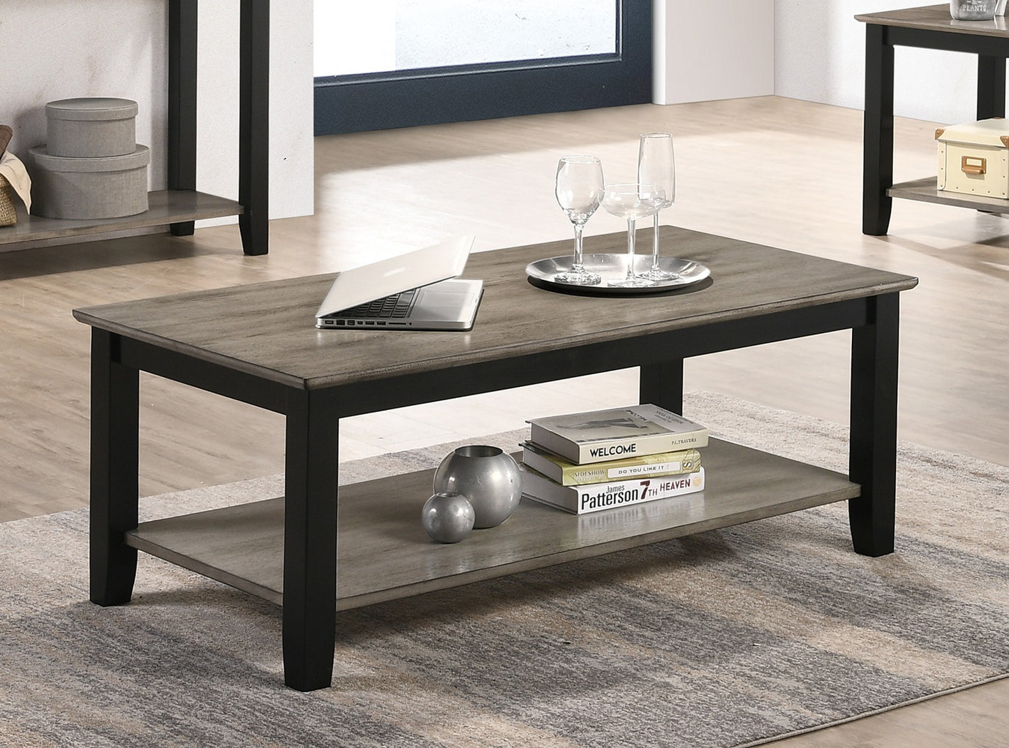 Modern gray wood coffee table with black frame and two tiers featuring a laptop and wine glasses