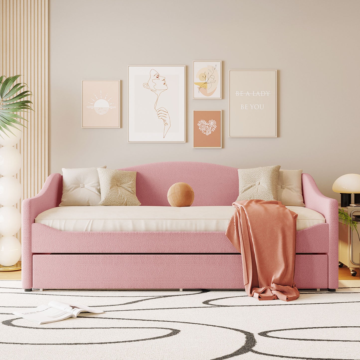 Pink upholstered daybed with plush throw pillows and a peach blanket