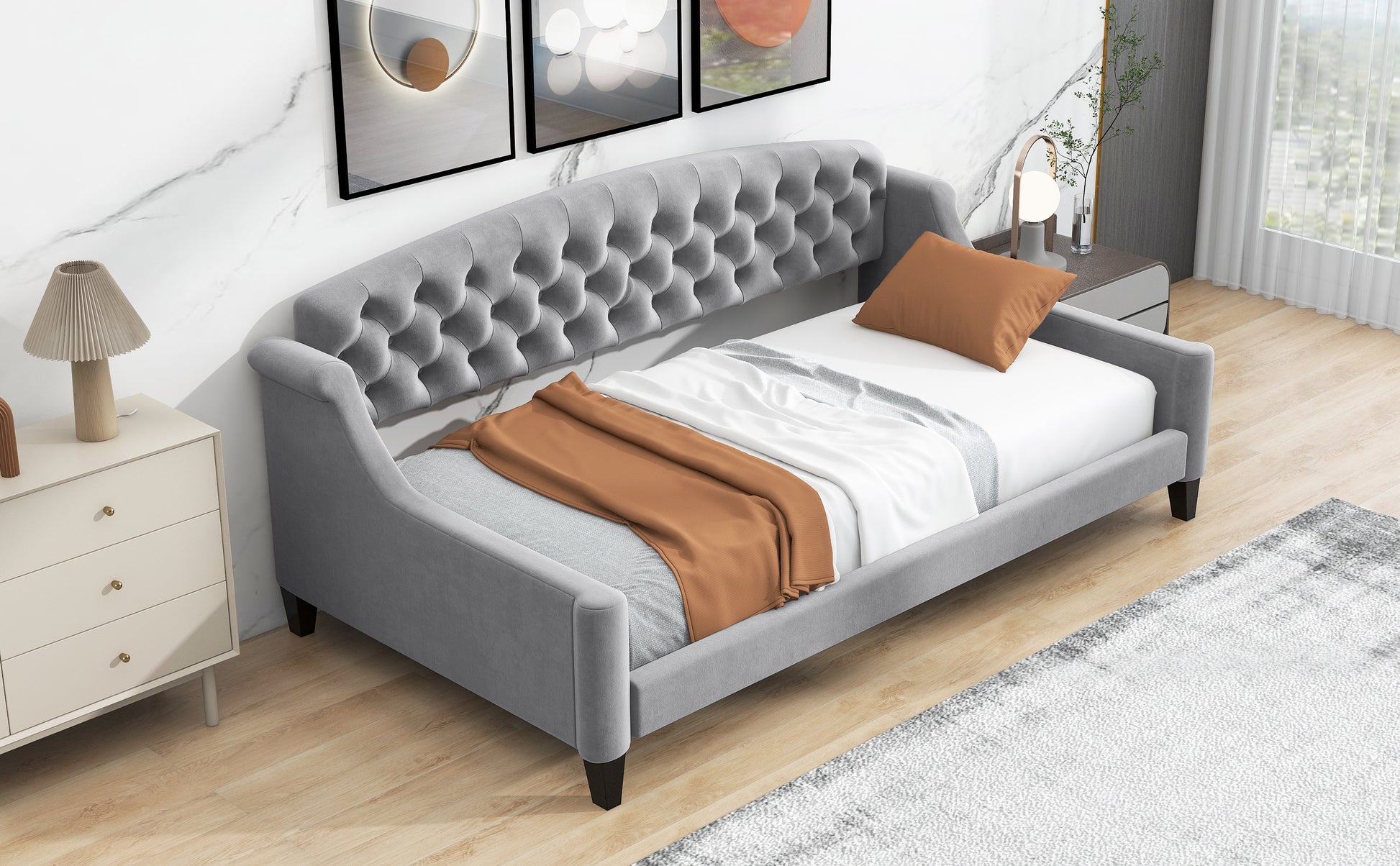 Grey tufted daybed with a burnt orange throw blanket and white linens